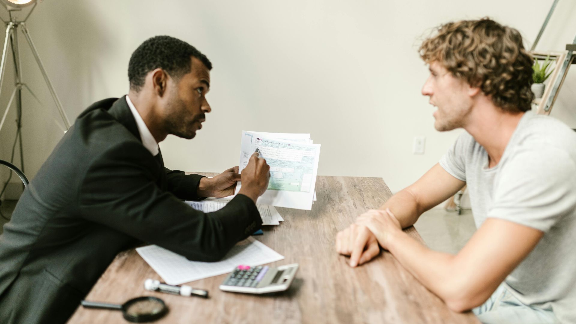A financial advisor discusses paperwork with a client at a desk in a modern office.