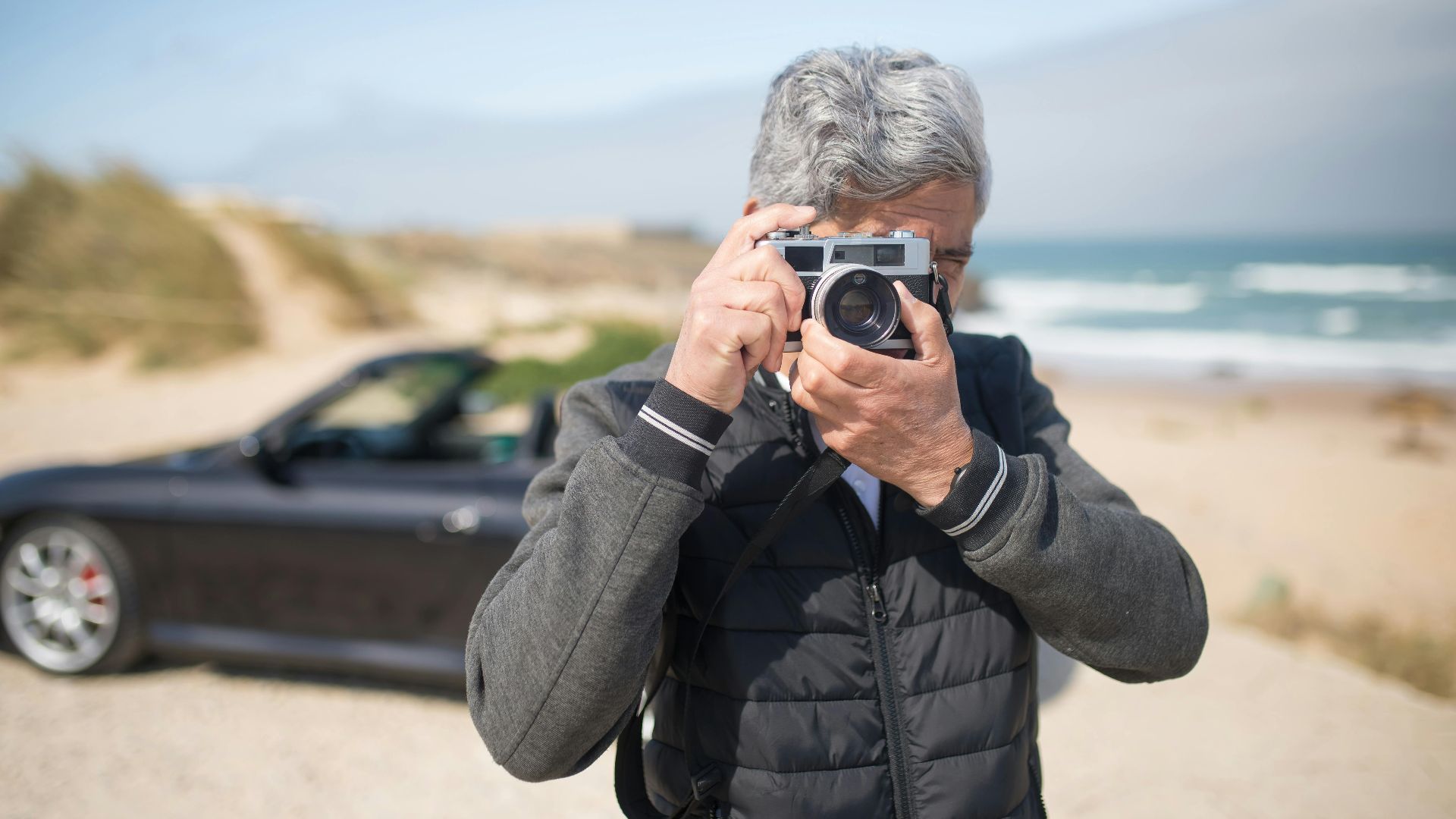 Senior man taking pictures by a scenic beach in Portugal with a vintage camera.
