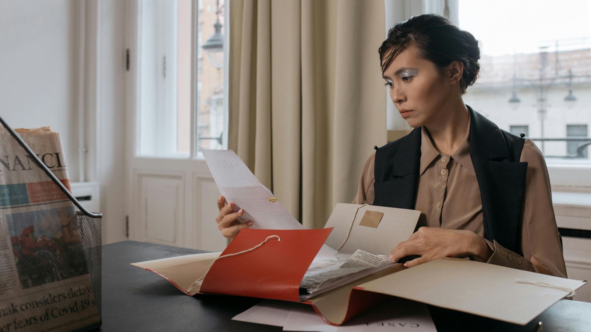 Businesswoman in an office setting reviewing important documents from a red folder with focus and determination.