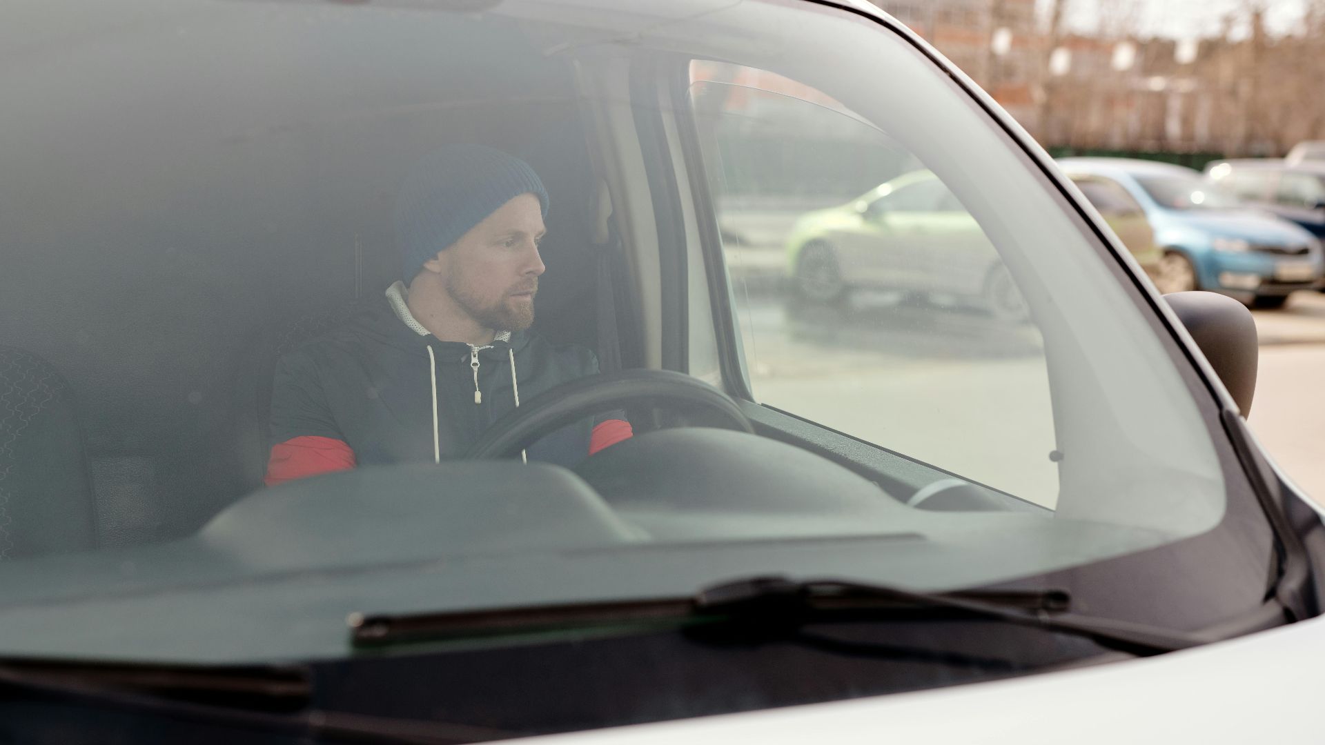 Man sitting in a van, focused on driving in an urban setting.