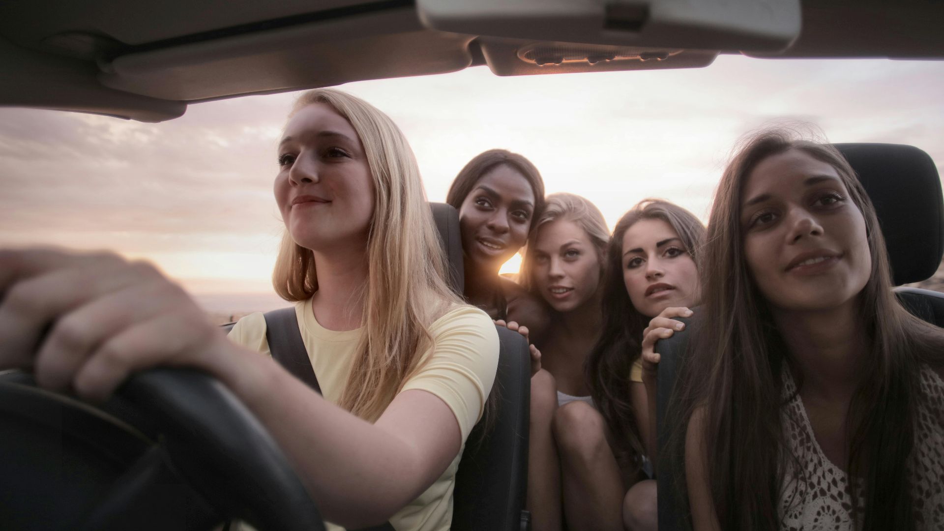Five women sharing a joyful road trip at sunset, symbolizing friendship and adventure.