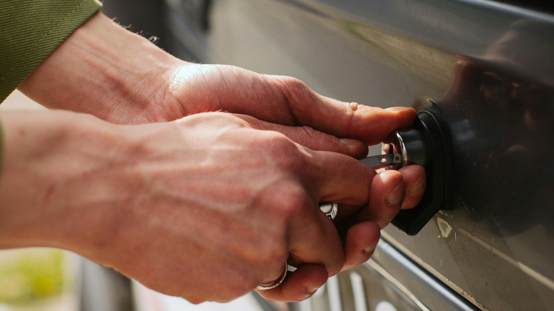 Close-up of hands unlocking a vehicle trunk with a key, showing detail and reflection.