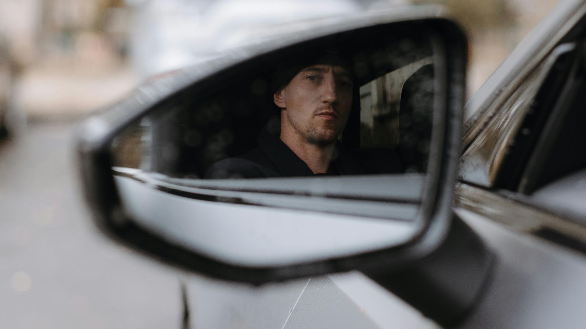 A man's reflection in a car side mirror with blurred background cars.