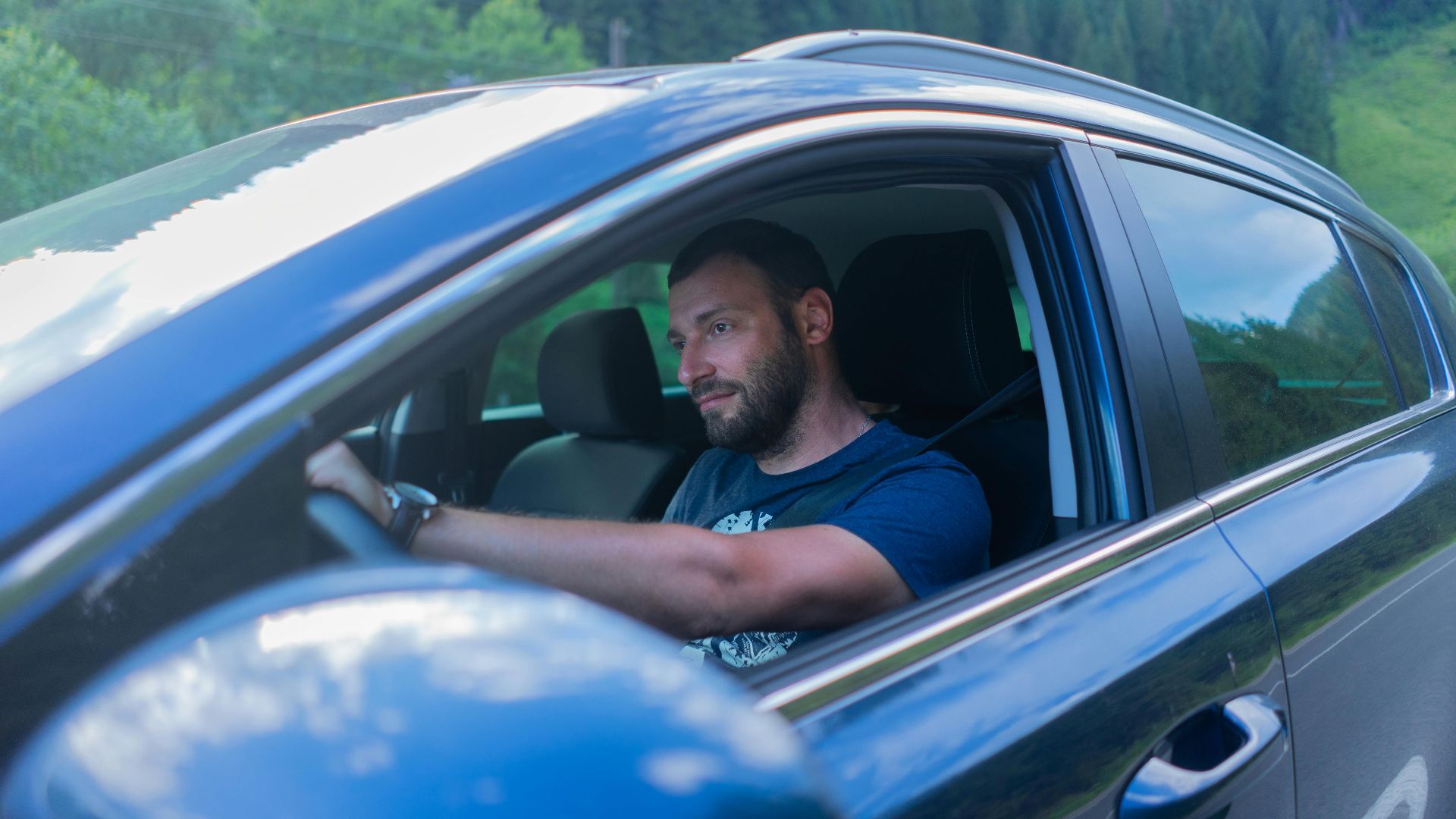 Bearded man enjoying a drive through lush green countryside on a sunny day.