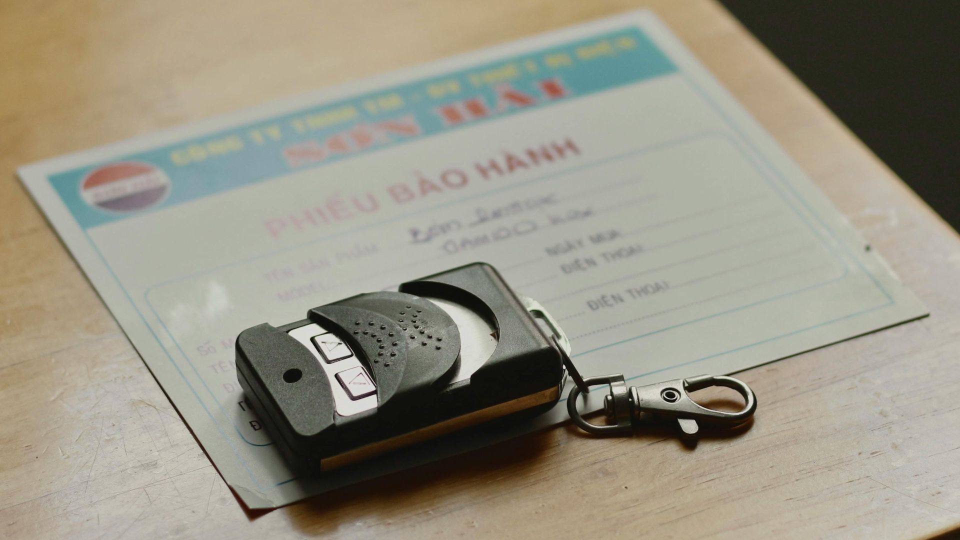 Remote control device resting on a warranty document placed on a wooden table.