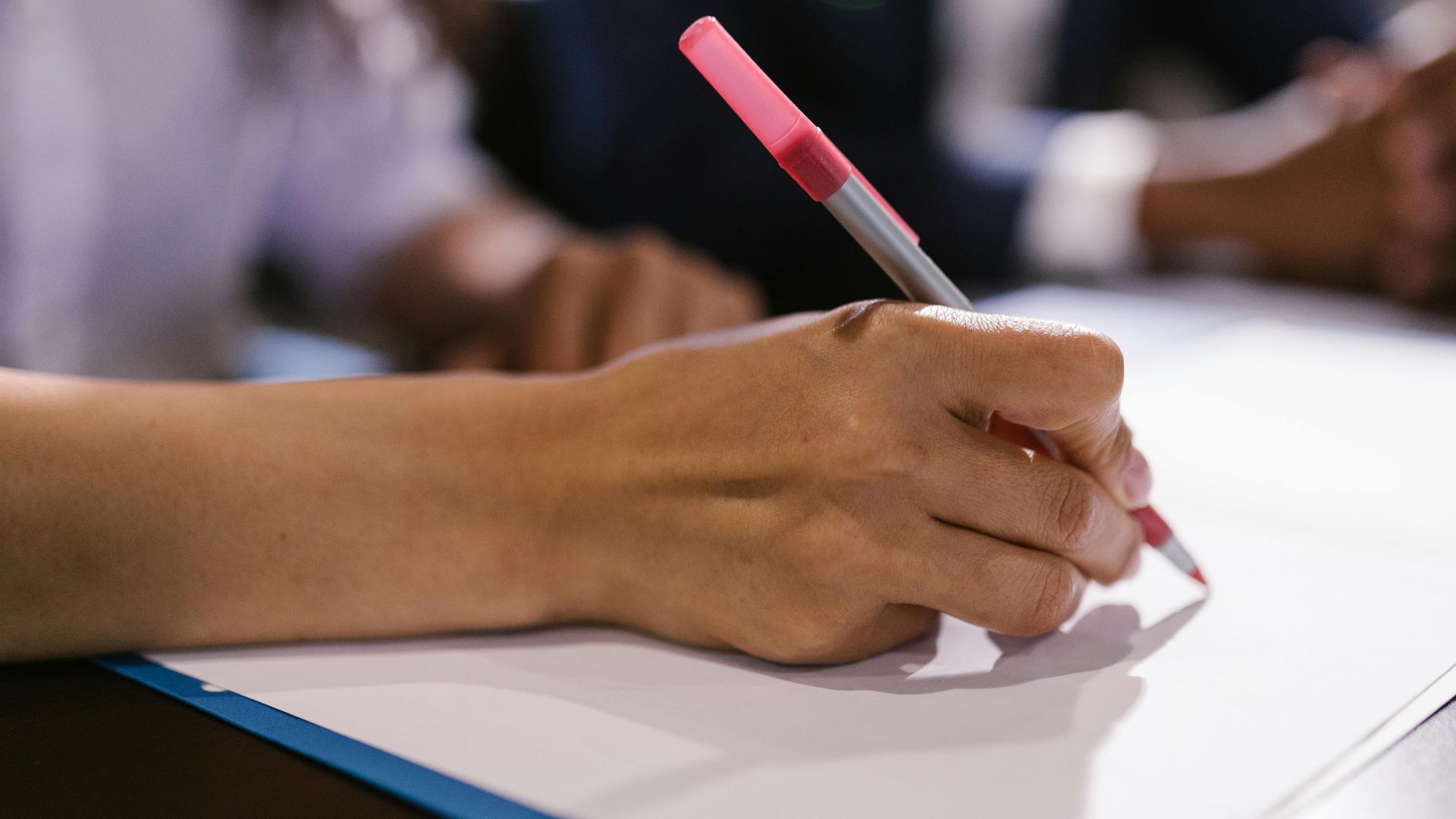 Detailed close-up of a person writing on paper with a pen in an office setting.