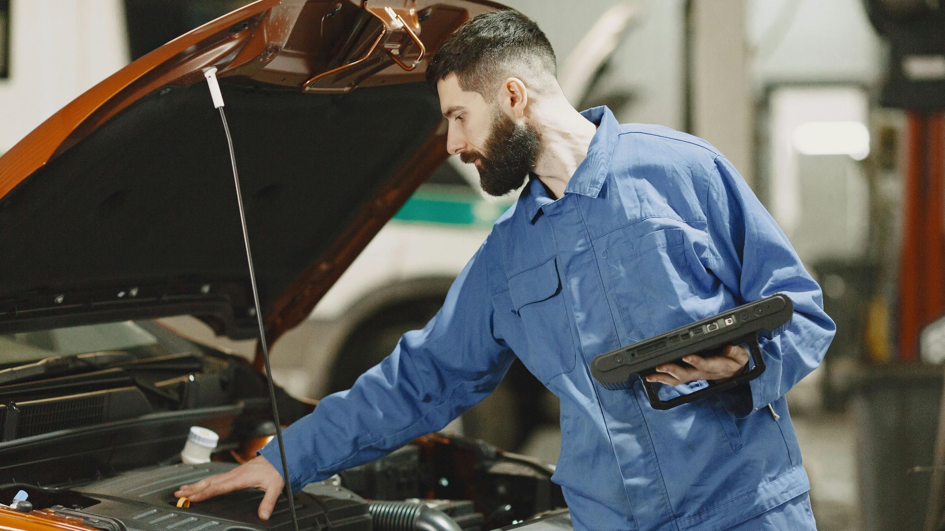 Professional mechanic examining a car engine under an open hood in a garage setting.