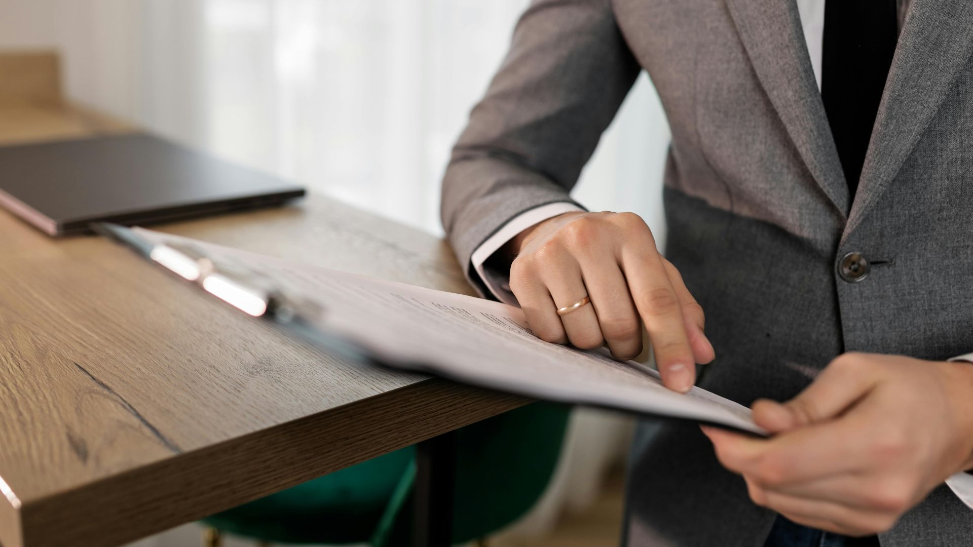 Professional businessman in suit reviewing documents on clipboard at office desk.