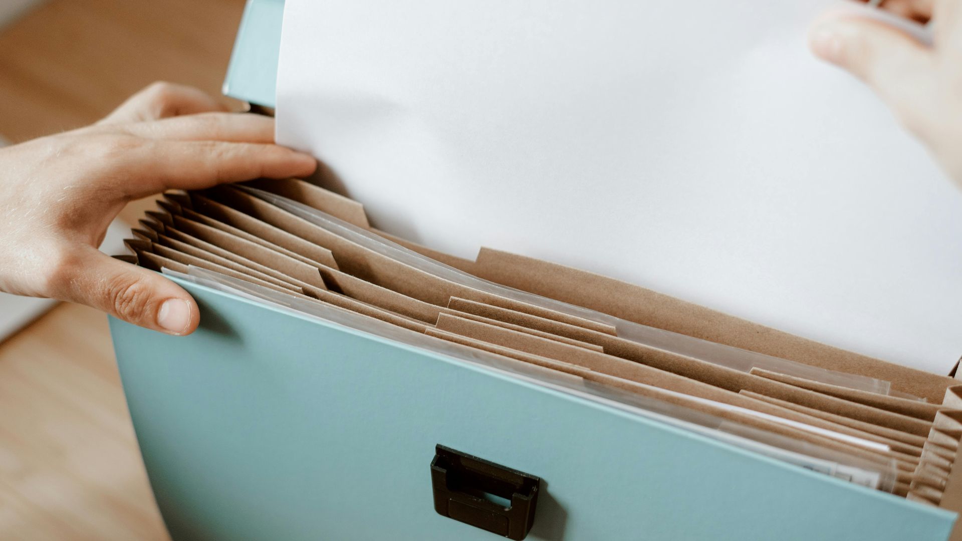 Crop faceless person putting sheet of paper in briefcase for documents placed on table