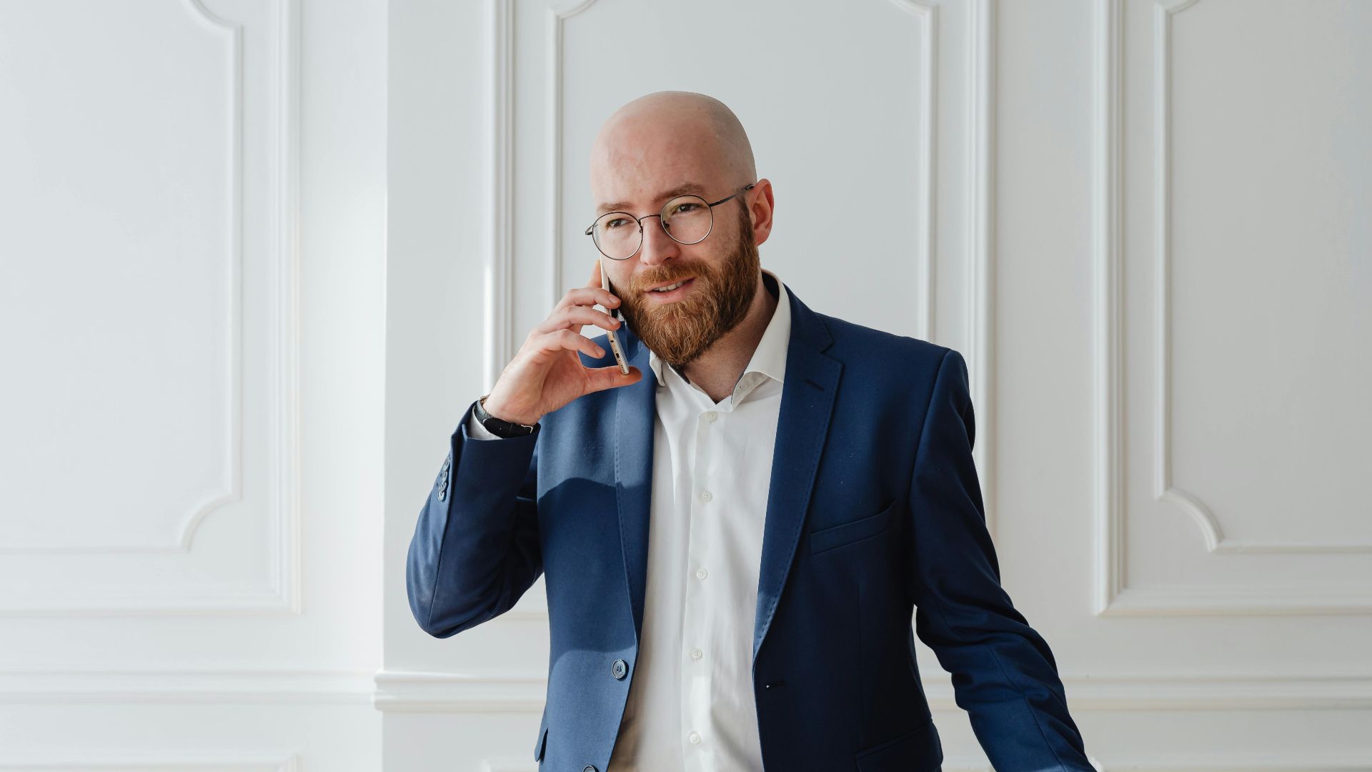 Bald bearded businessman in a suit having a phone call indoors.