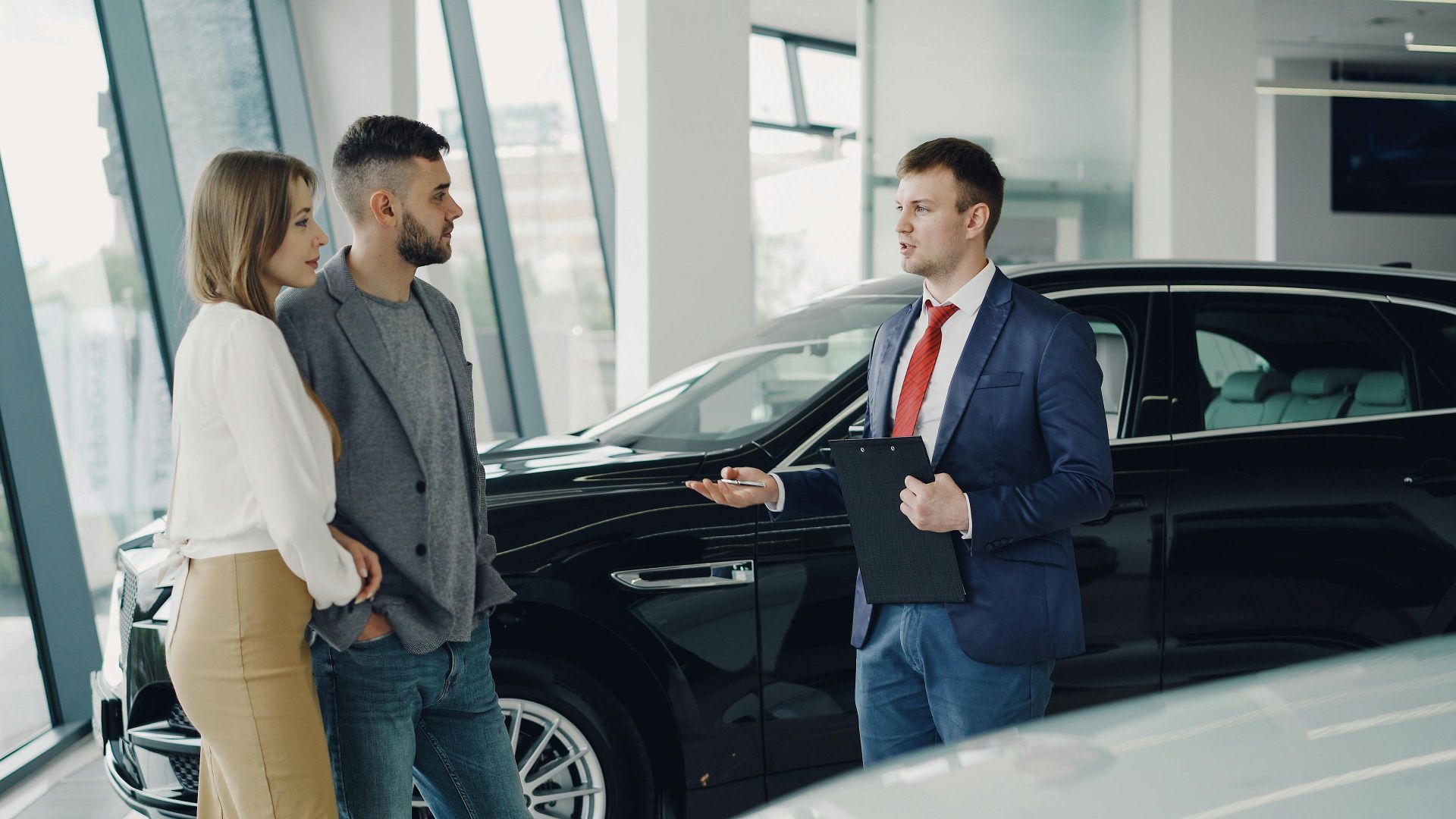 A couple talks with a salesman in a modern car showroom, considering a vehicle purchase.