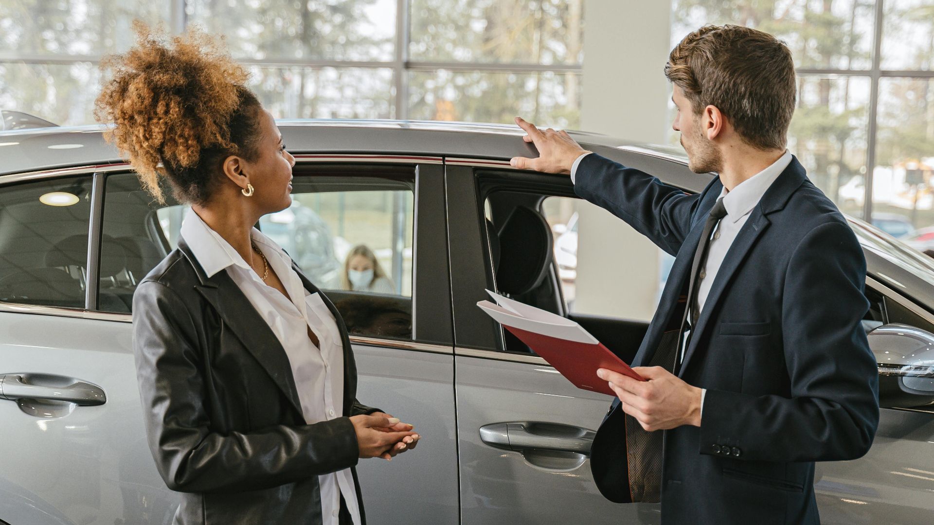 A woman and a car salesman discuss vehicle options inside a dealership.