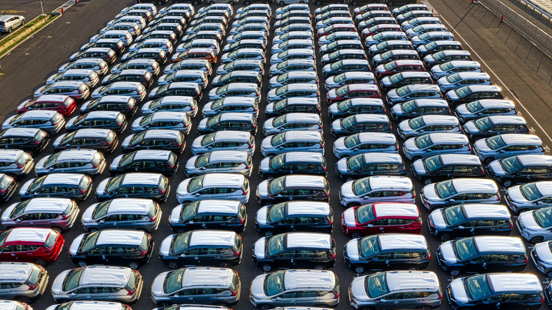 From above of many modern new automobiles placed on asphalt near factory in daytime