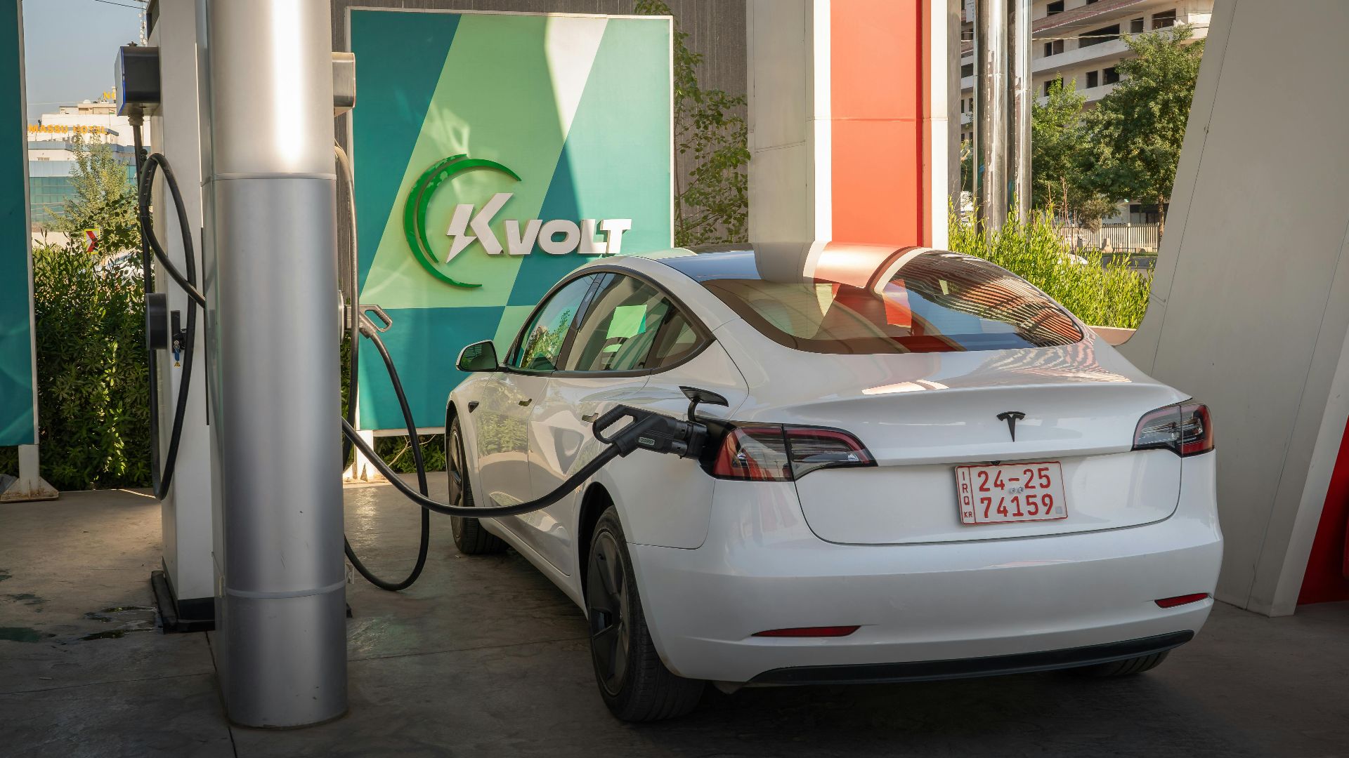 A white Tesla Model 3 charging at an outdoor electric vehicle station with Kvolt branding.