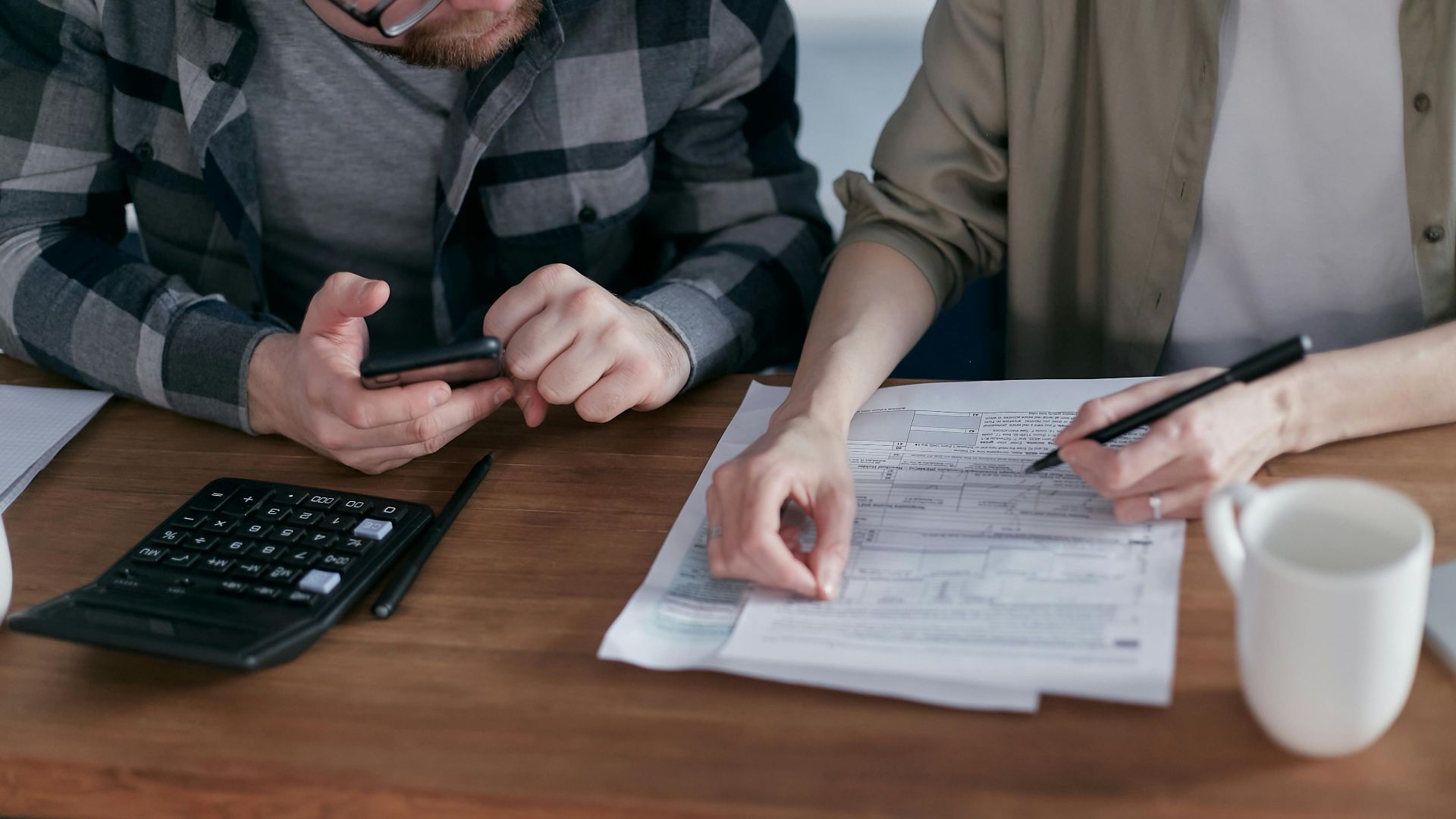 A couple diligently reviews their finances using a calculator and documents at home.