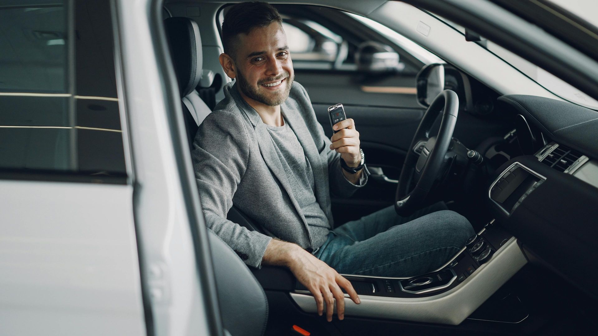 Happy man holding car keys while seated inside a modern vehicle.