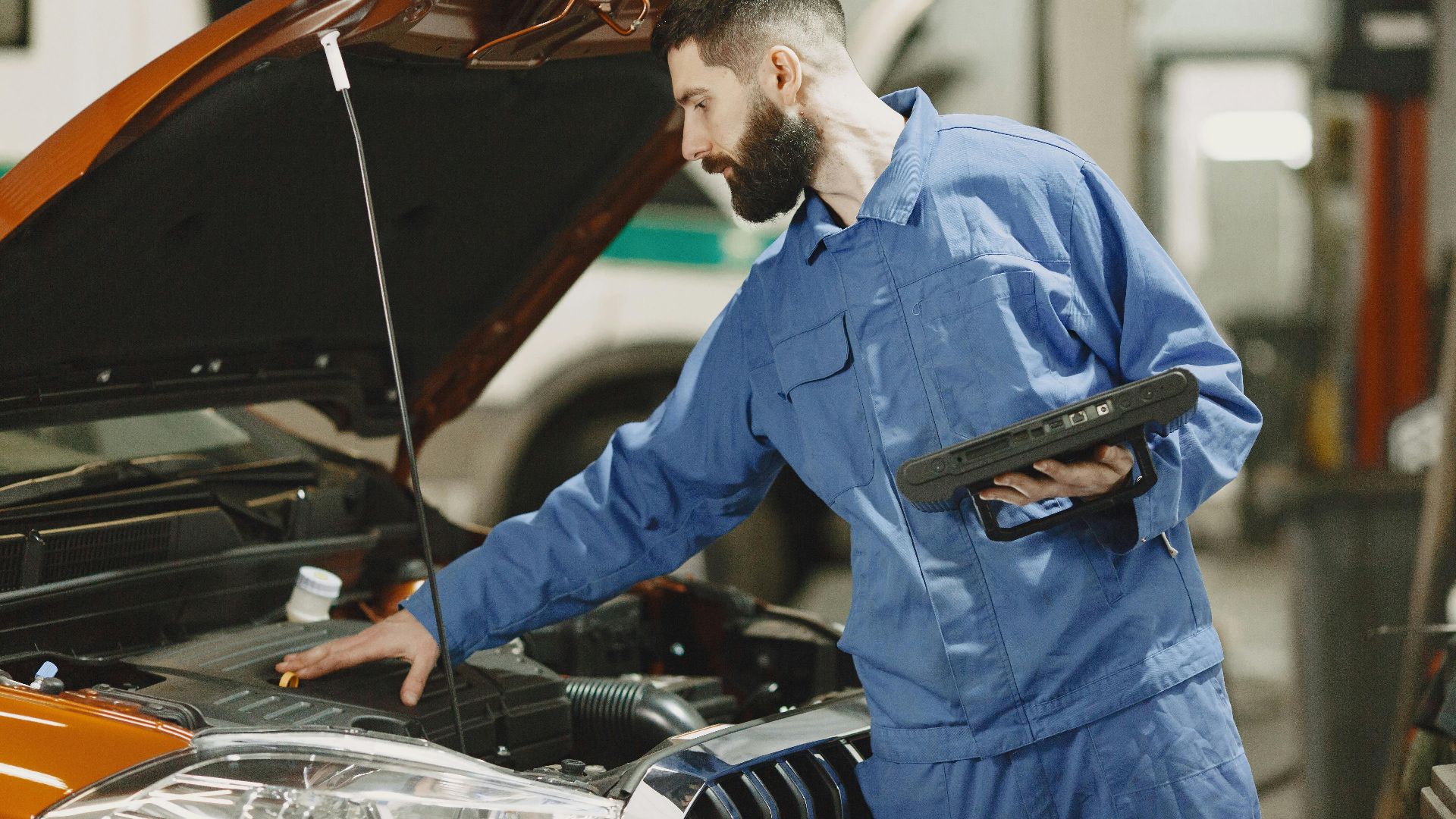 Professional mechanic examining a car engine under an open hood in a garage setting.