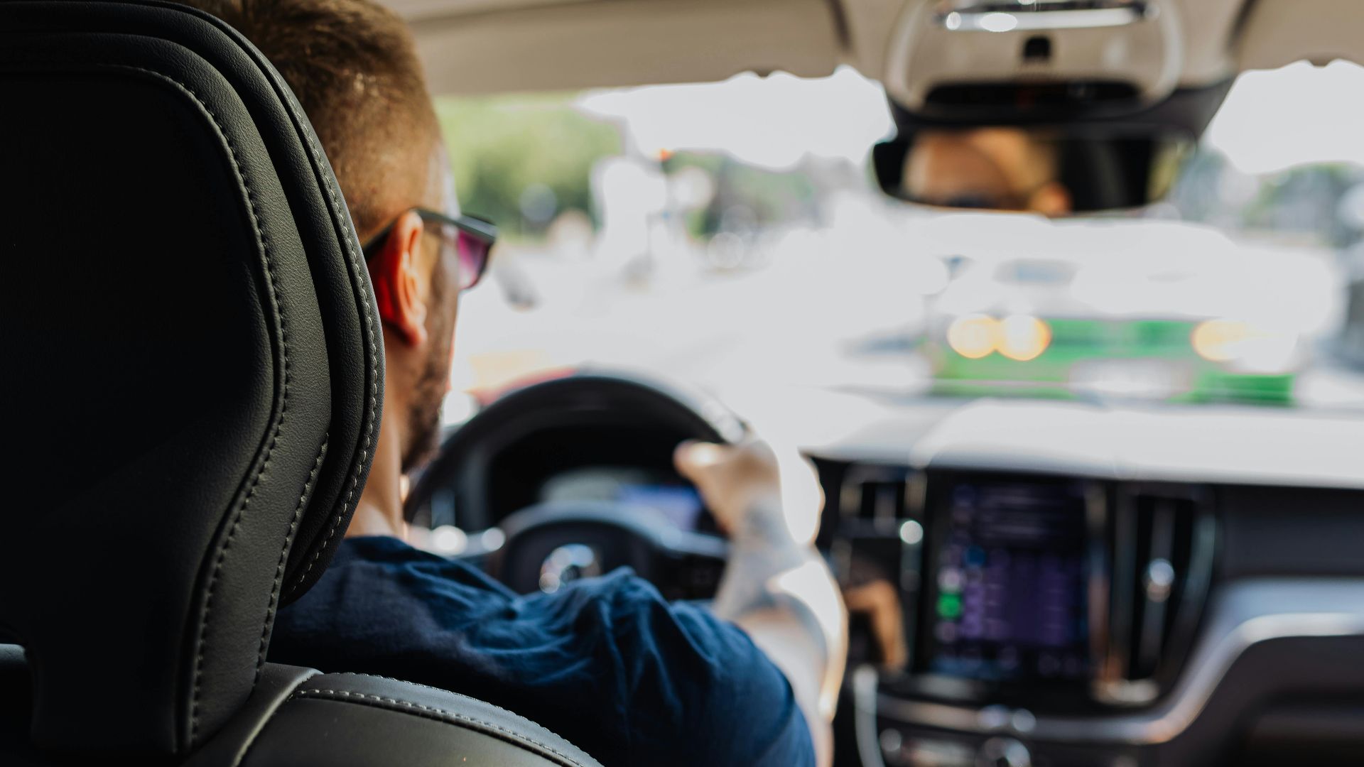Close-up of a man driving a modern vehicle from behind with a blurred urban background.