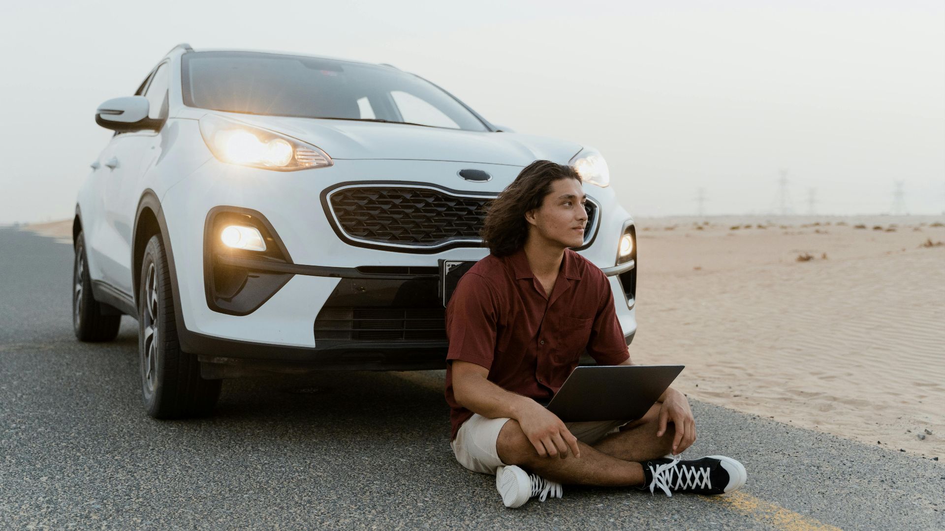 A man with a laptop sitting by an SUV on a desert road, working remotely.