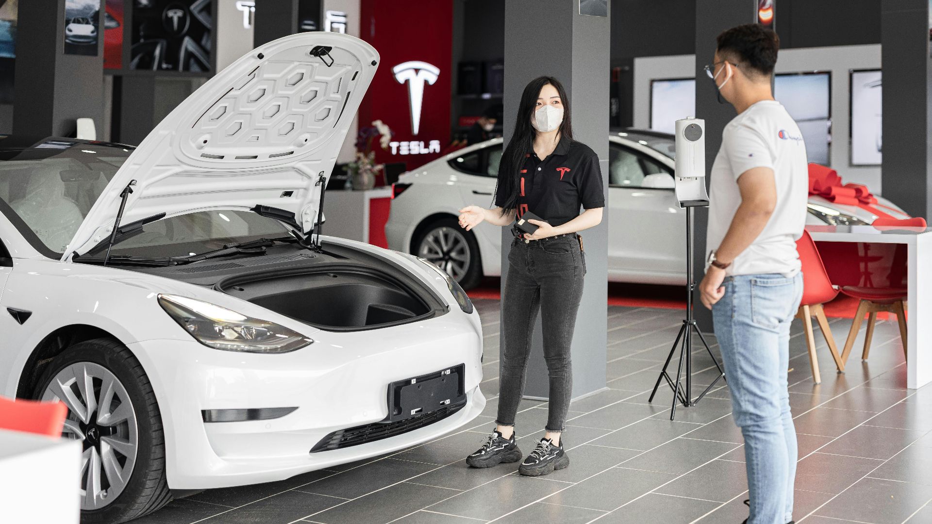 A customer talks with a sales representative about a Tesla Model 3 in a car dealership, showcasing the electric car's features.