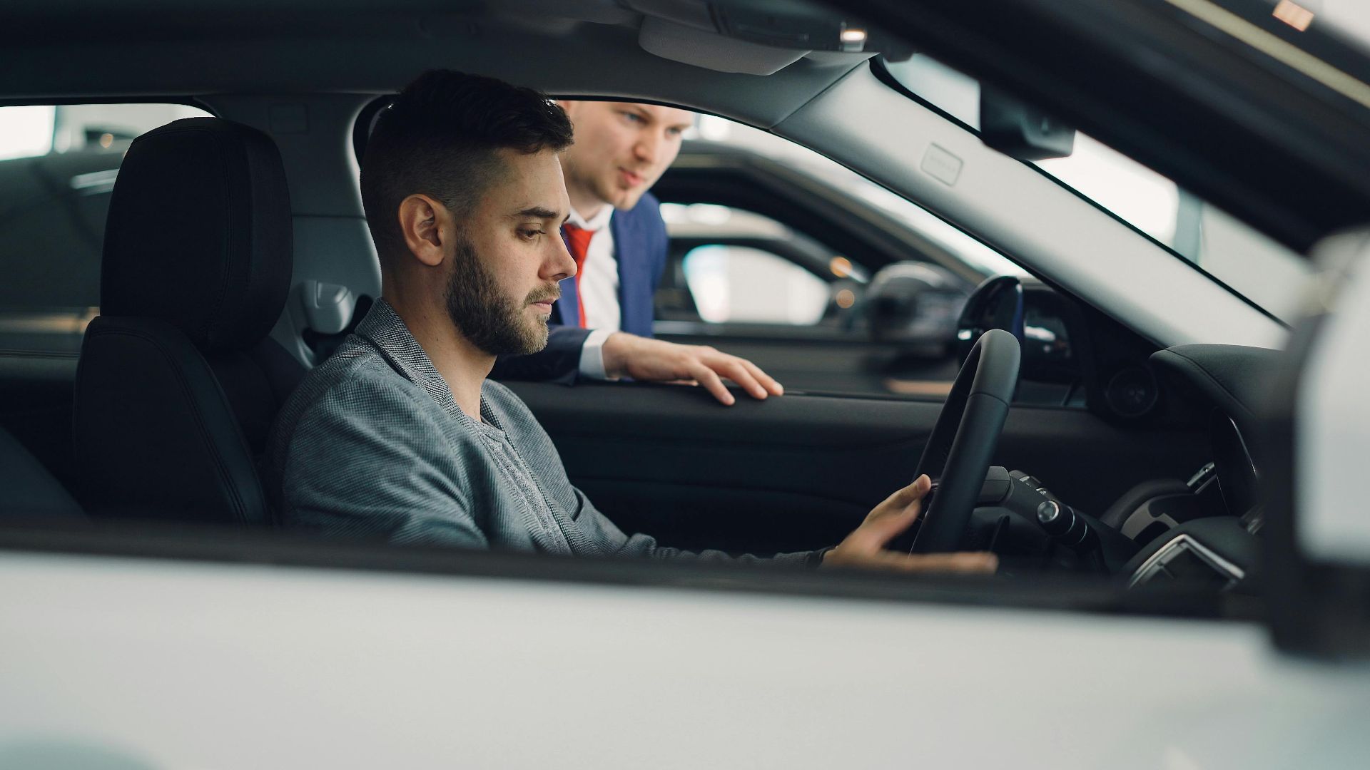 Man examining car interior with salesman at a dealership, highlighting car features.
