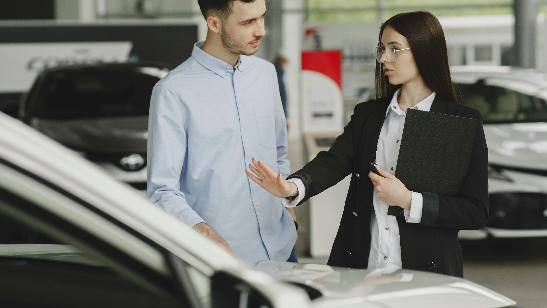 A salesperson and customer discussing car features in a dealership setting.