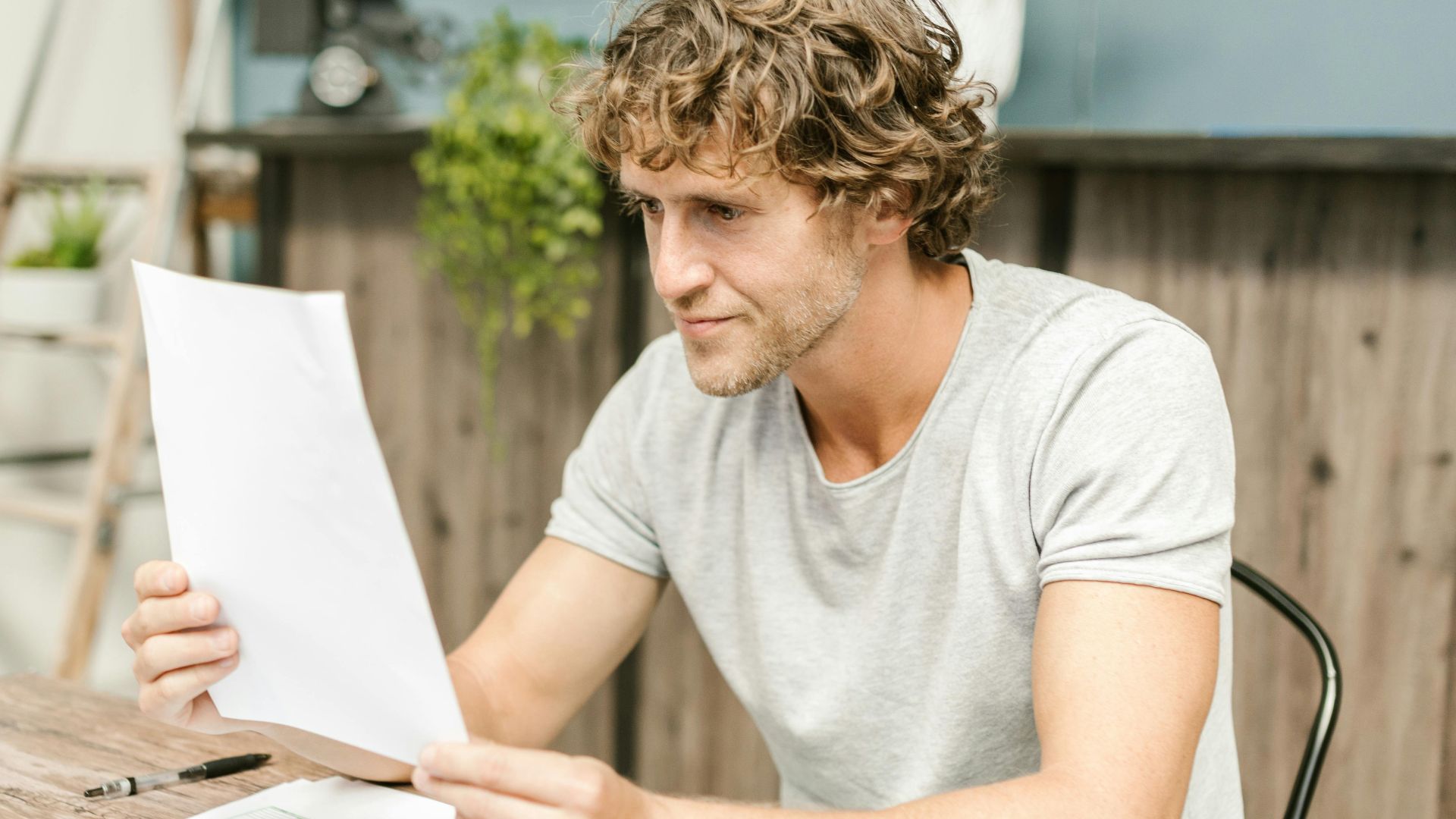 A man with curly hair evaluates documents at a desk, highlighting focused work in a professional setting.