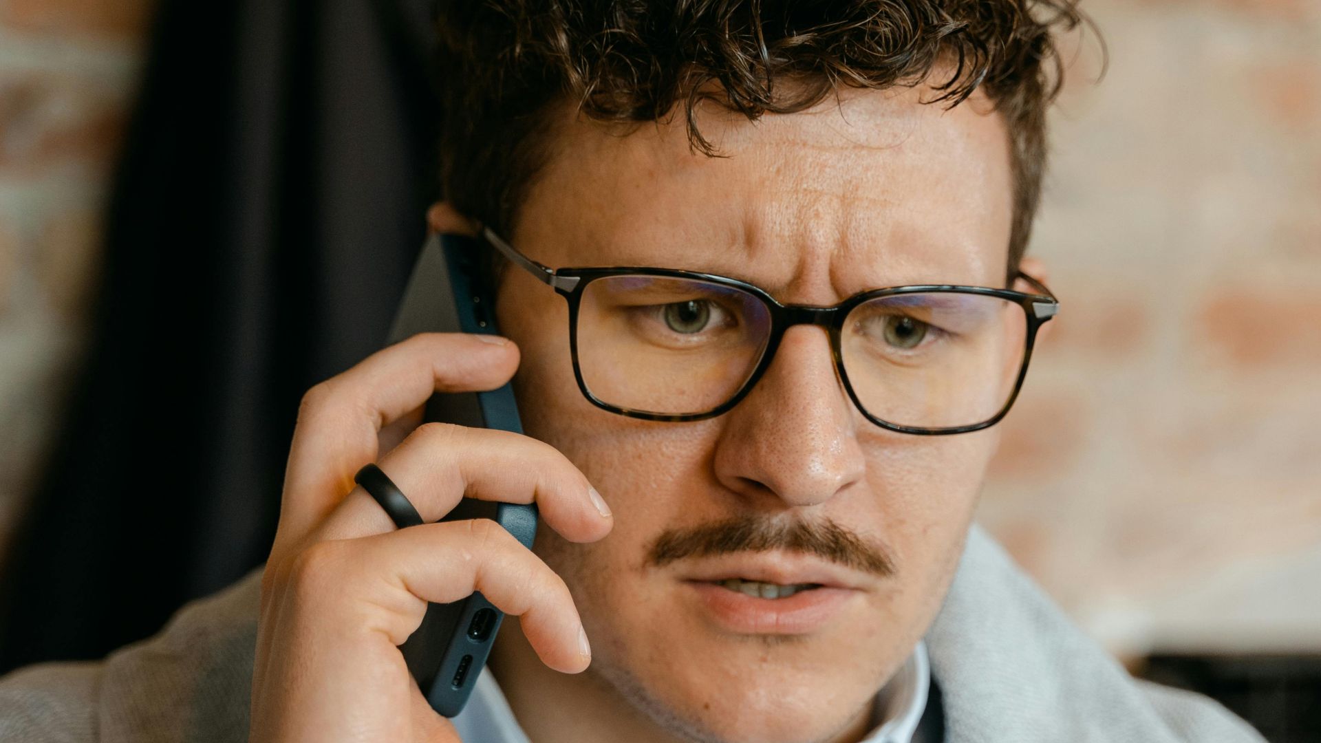 A man with curly hair and glasses engaged in a phone conversation indoors.