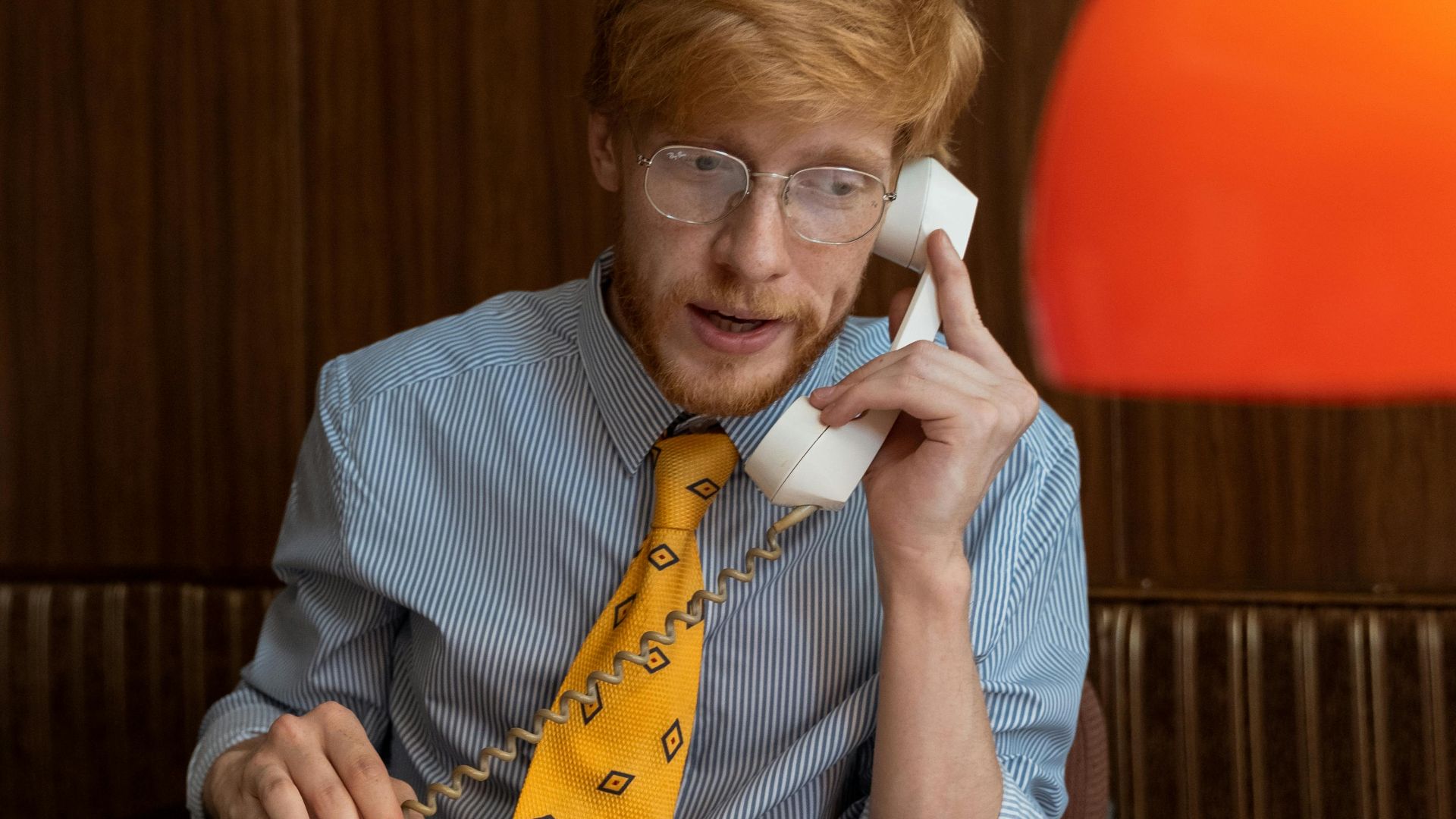 Caucasian man with red hair in retro office, talking on vintage telephone.