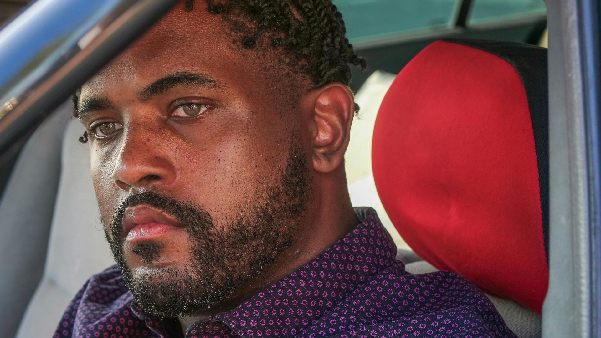 Close-up portrait of a man with facial hair sitting in a car staring intently.