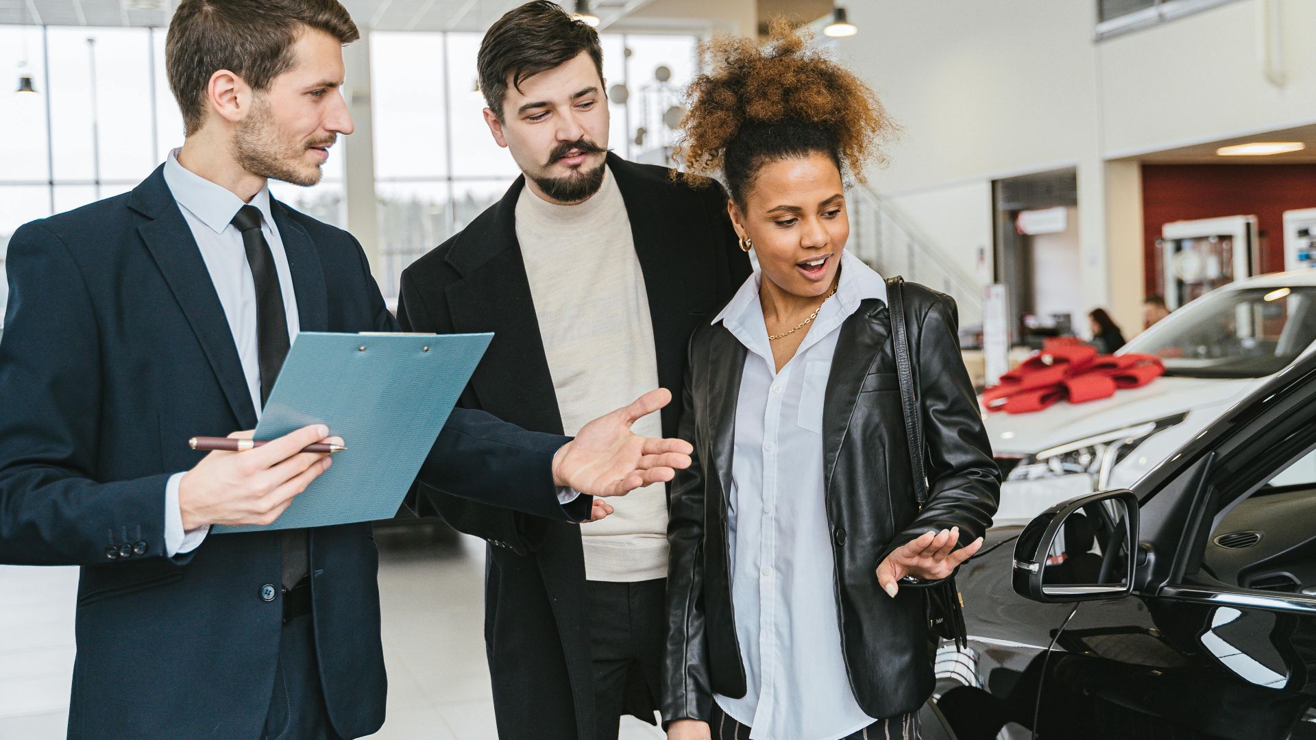 A diverse group of adults discussing vehicles at a bright modern car dealership.