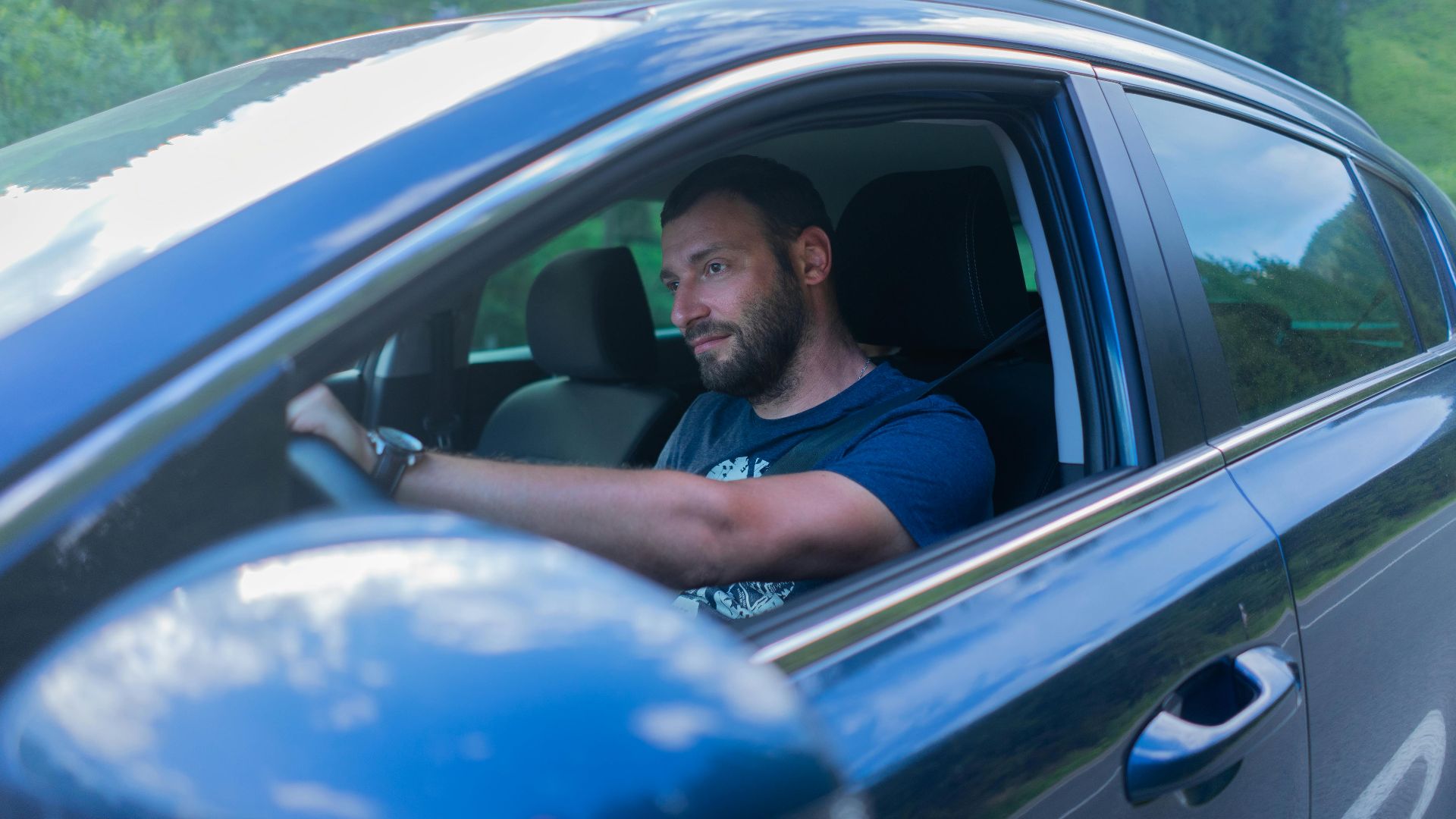 Bearded man enjoying a drive through lush green countryside on a sunny day.