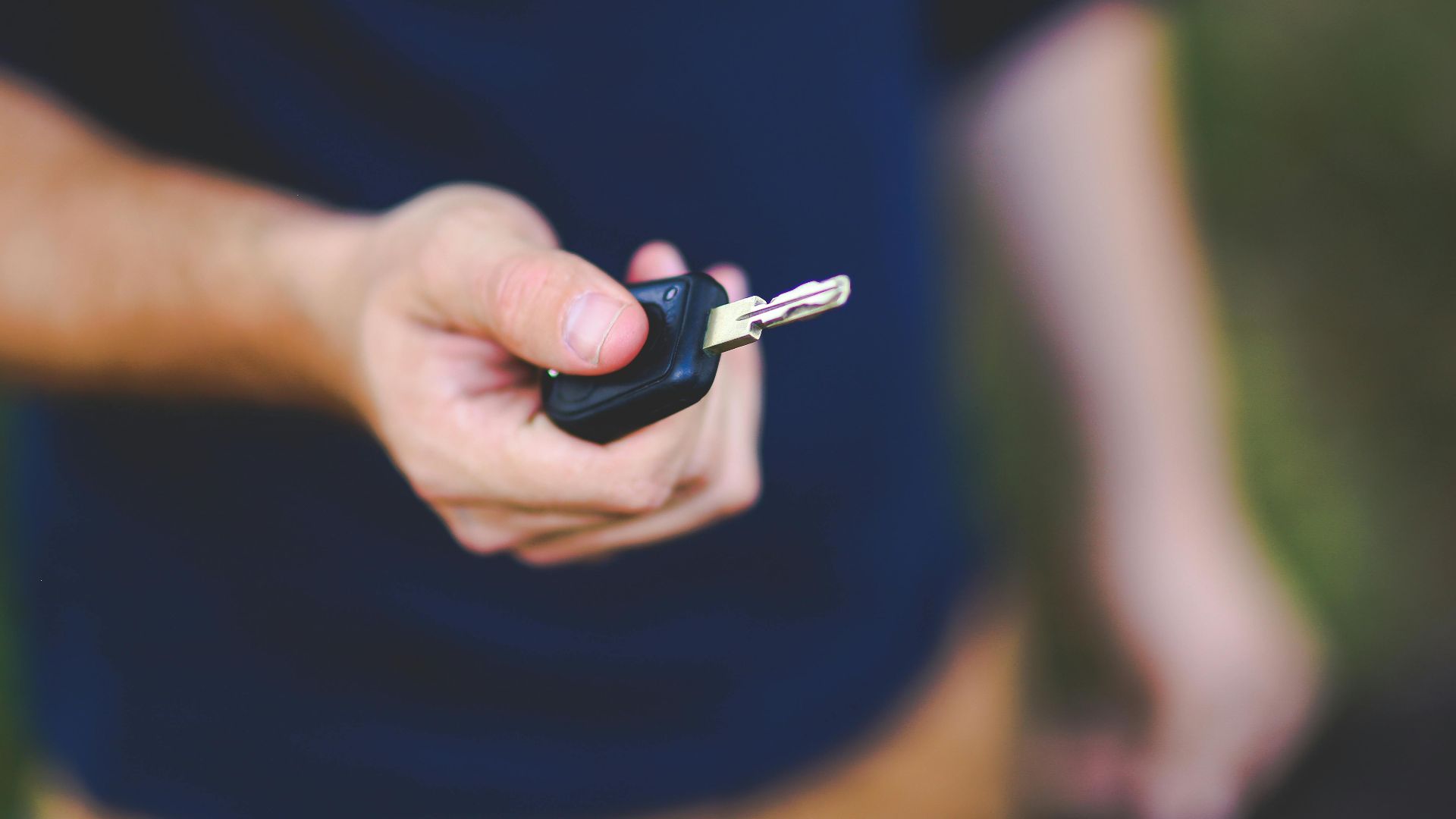 A hand holding a car key outdoors, emphasizing security and control.