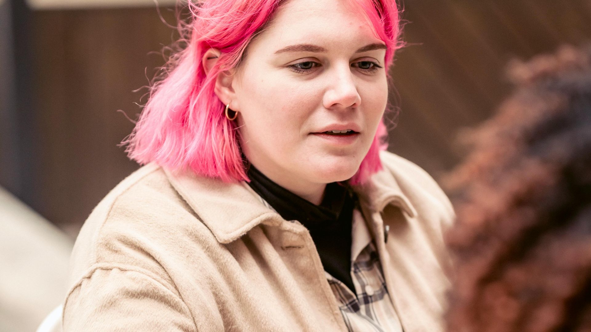 Young female with pink hair sitting at table and talking with friend on weekend day in street cafeteria