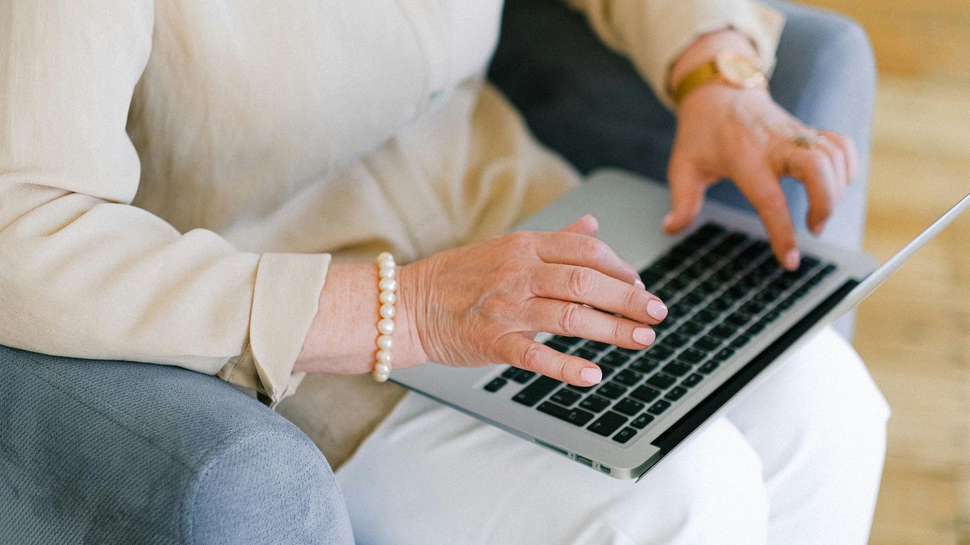 From above of crop anonymous elderly female typing information for report on netbook while resting in armchair in living room