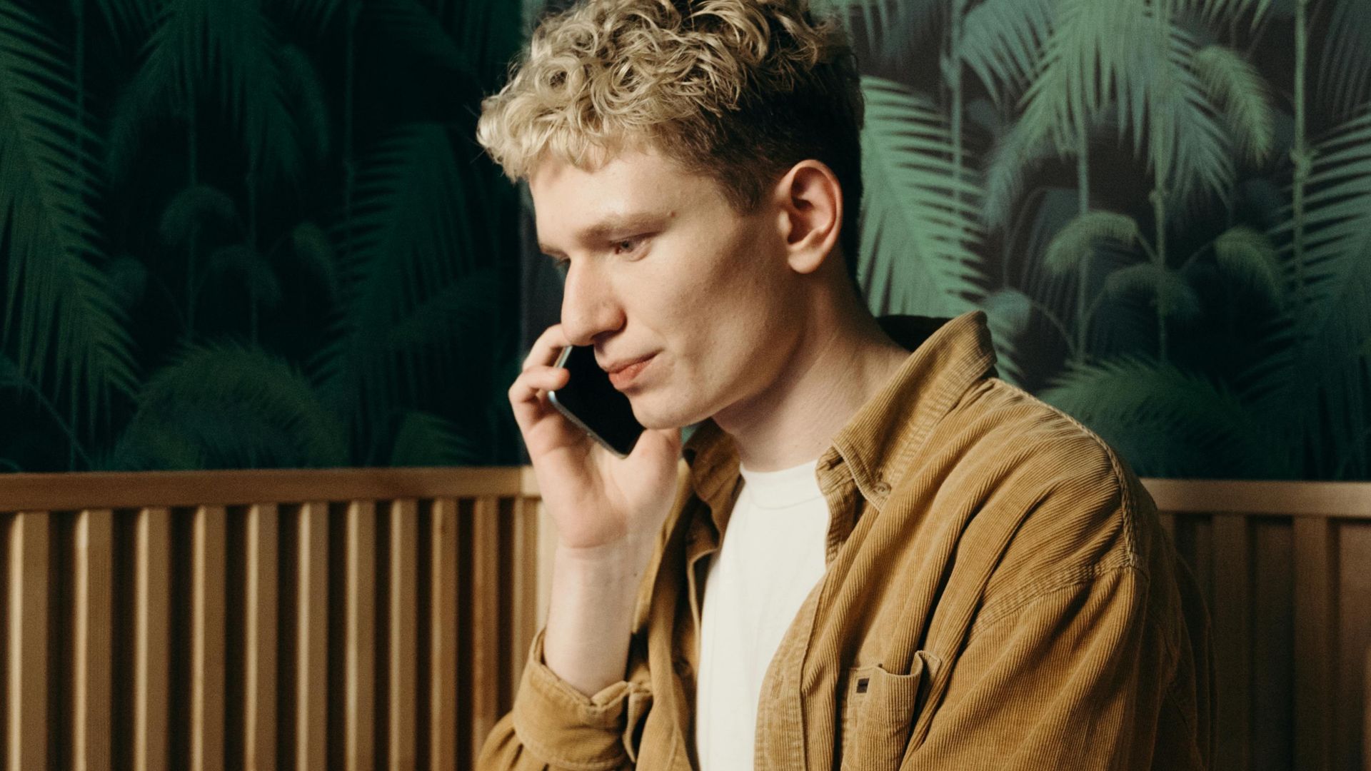A young man working on a laptop while talking on the phone in a stylish cafe.