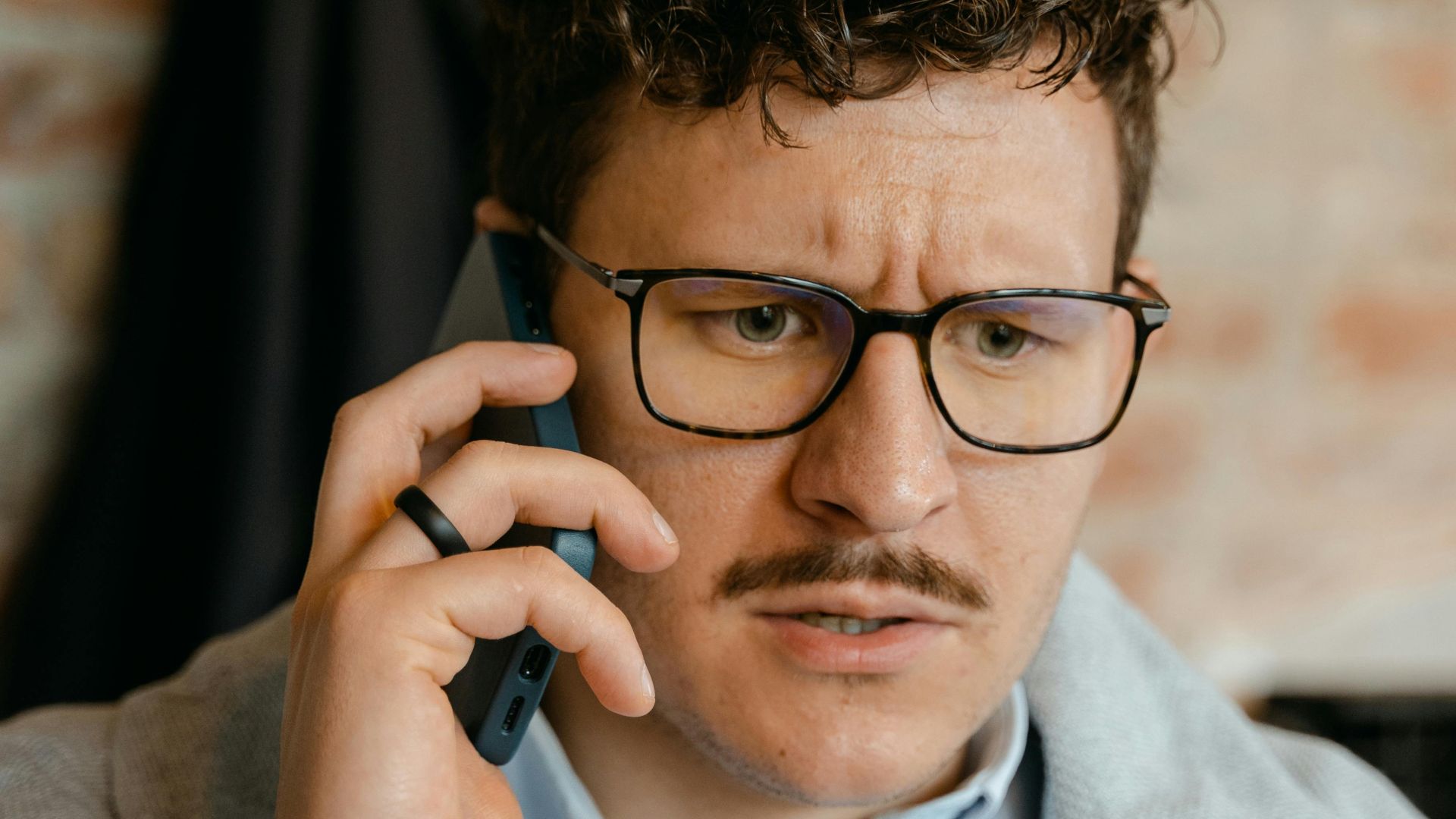 A man with curly hair and glasses engaged in a phone conversation indoors.