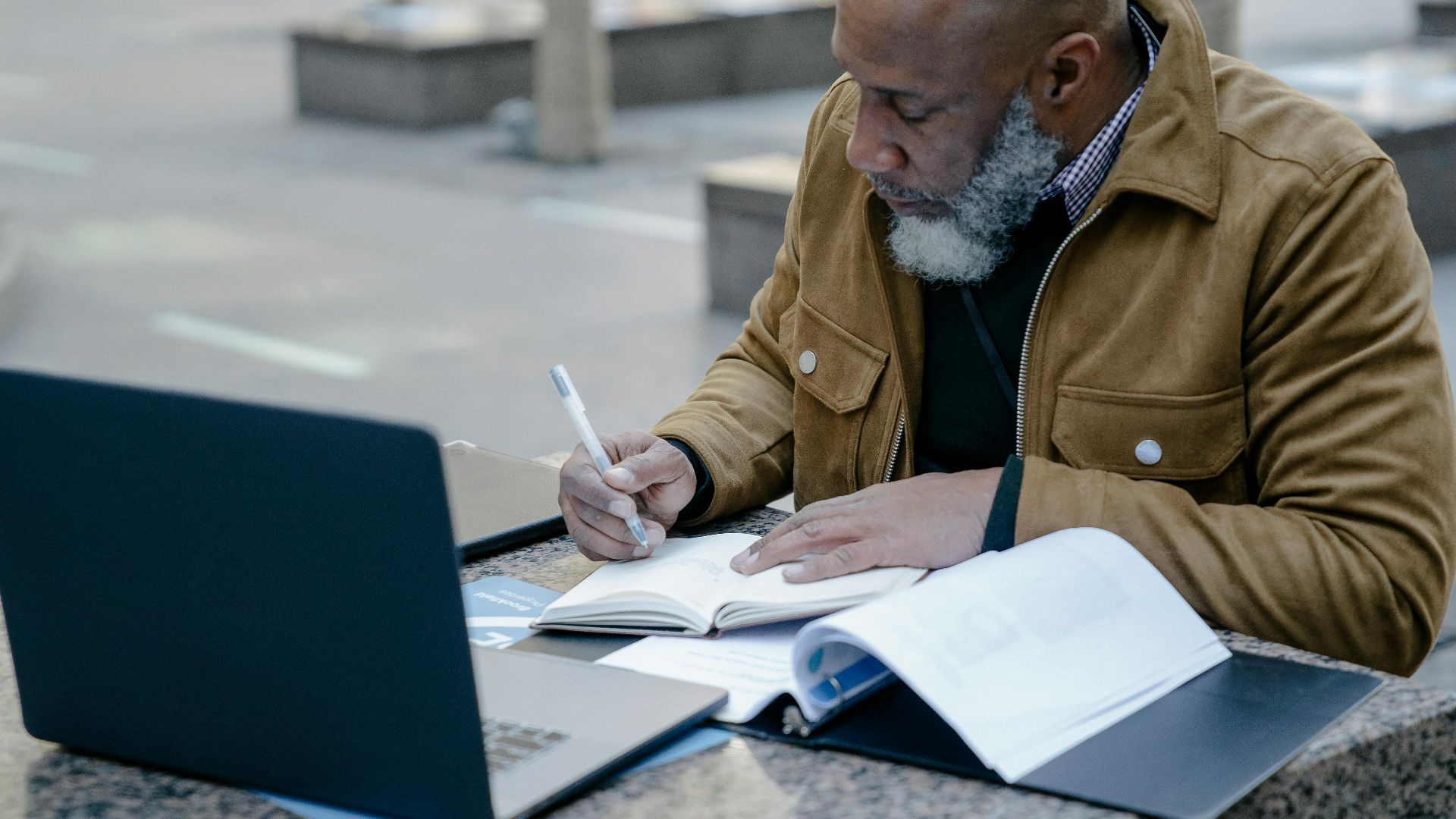 Mature man working with laptop and notebook outdoors, focusing on business tasks.