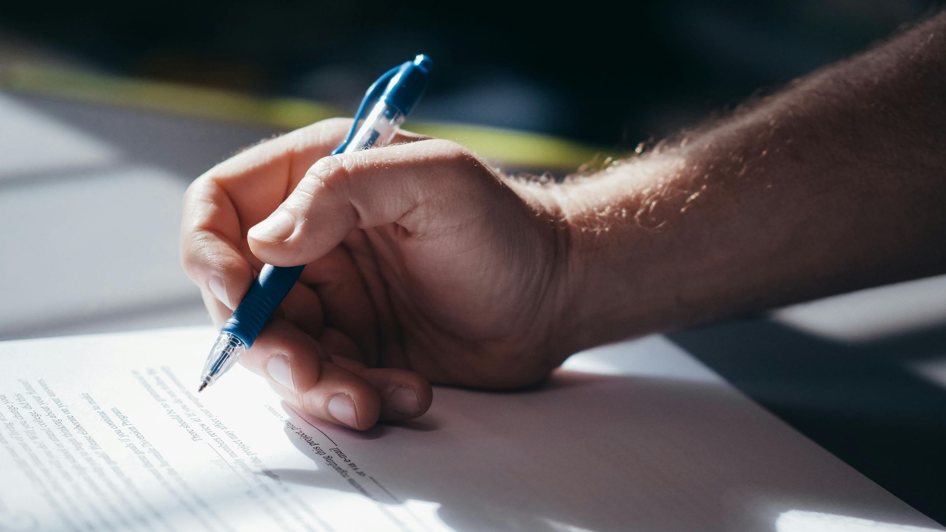 Detailed shot of a hand holding a blue pen while signing a document. Ideal for legal and business themes.