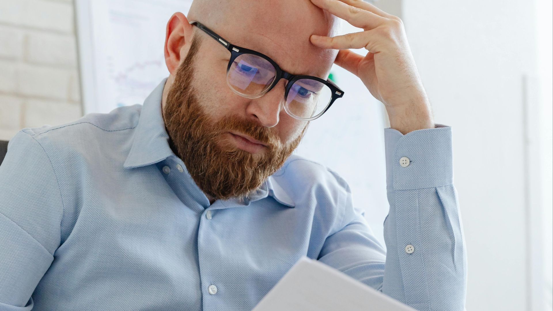 Caucasian businessman with beard and glasses reviewing documents in a modern office setting.