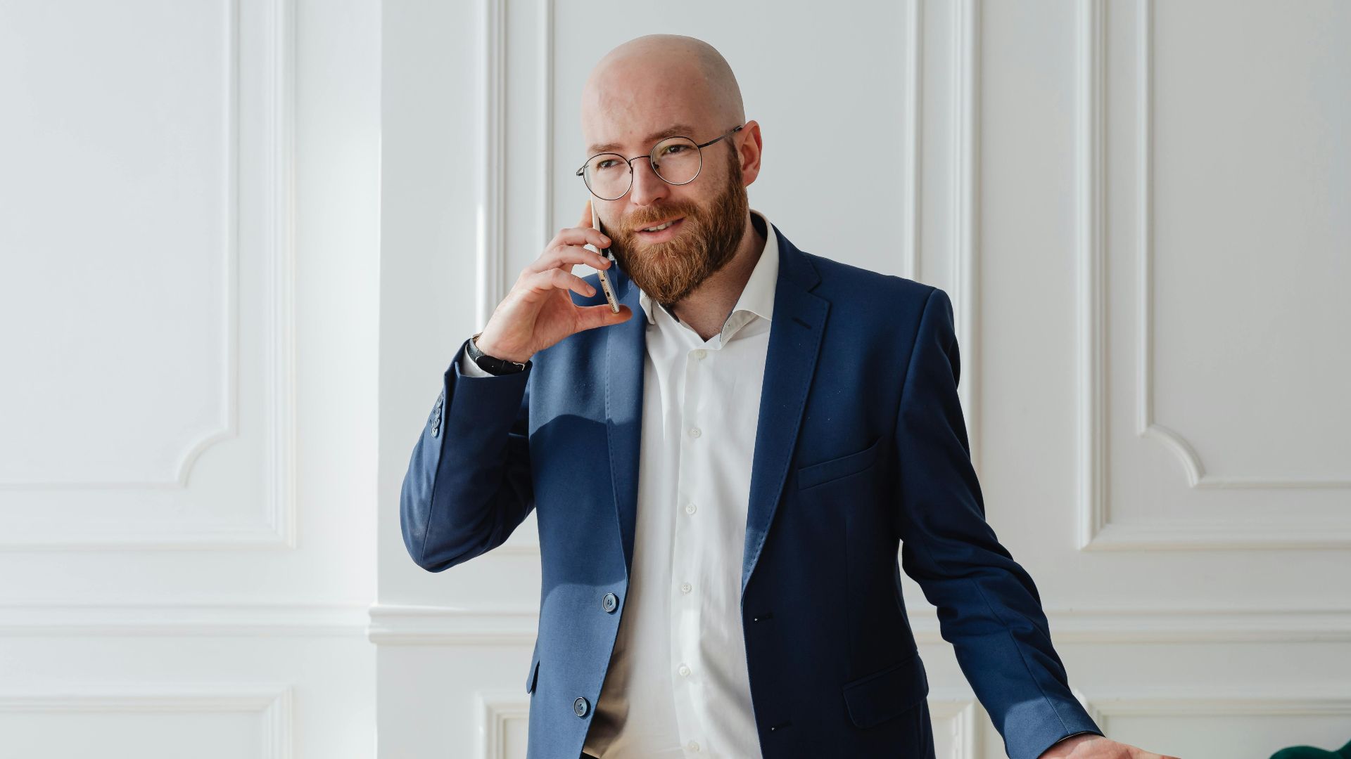 Bald bearded businessman in a suit having a phone call indoors.