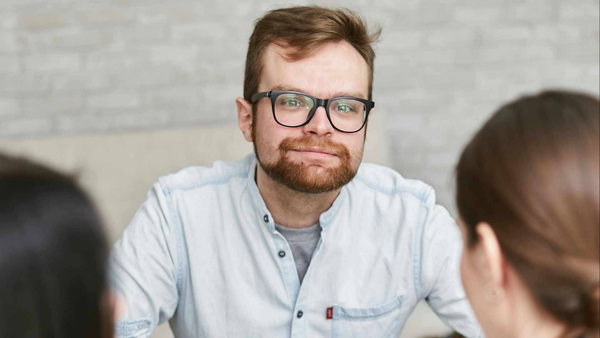 A man in glasses leads a meeting discussing documents with two women.
