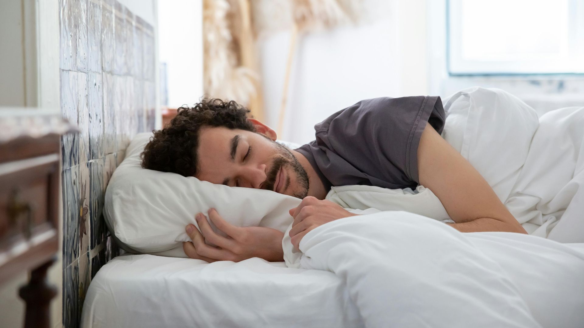 Man resting peacefully in bed, wrapped in white sheets, creating a serene and cozy atmosphere.