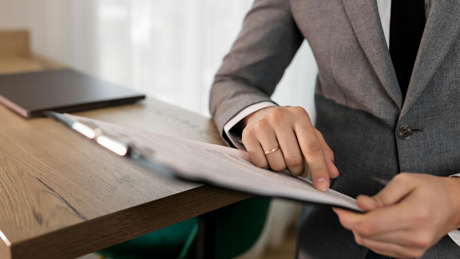 Professional businessman in suit reviewing documents on clipboard at office desk.