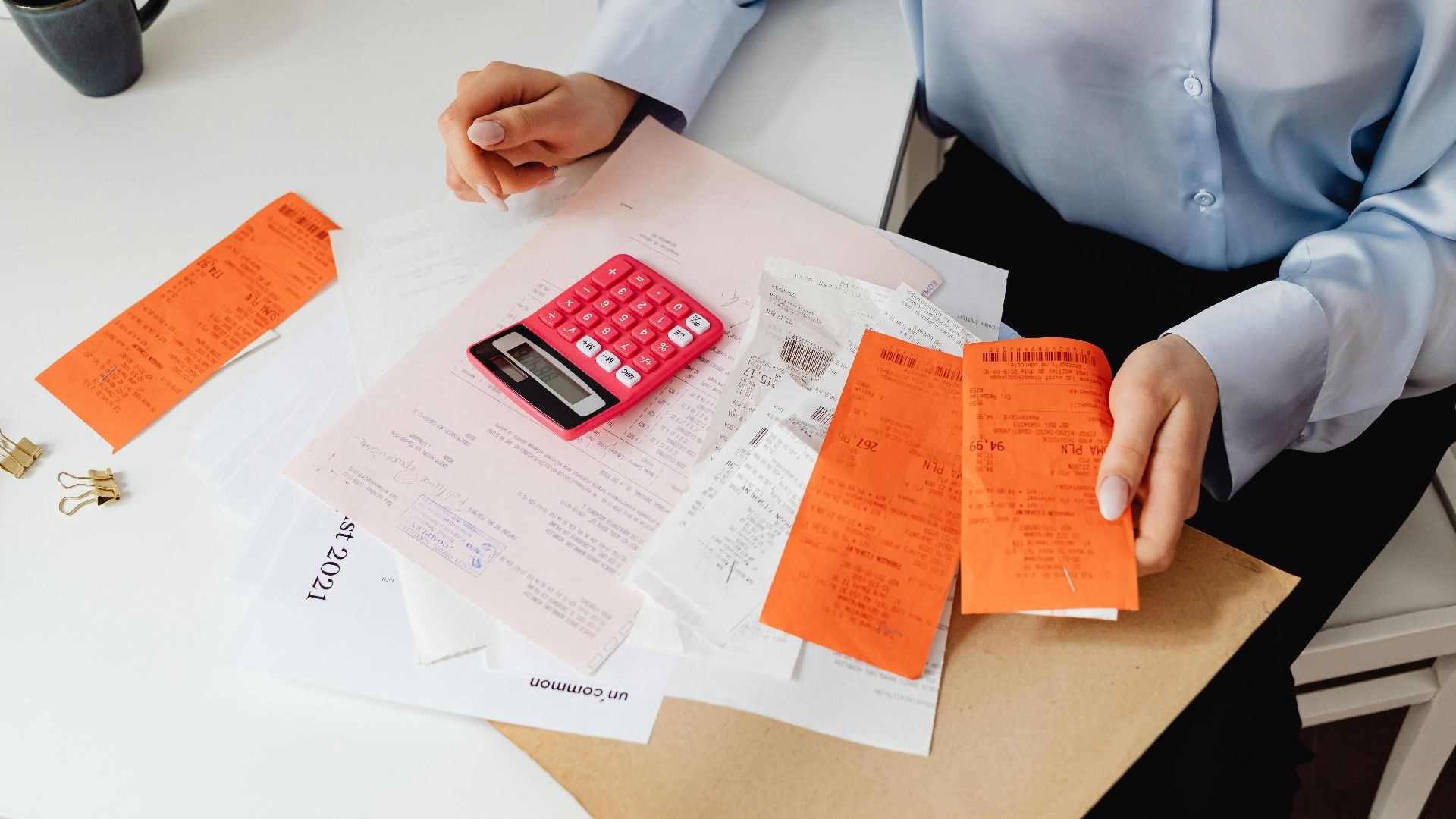 A woman reviews receipts and calculates expenses at a desk with a pink calculator.