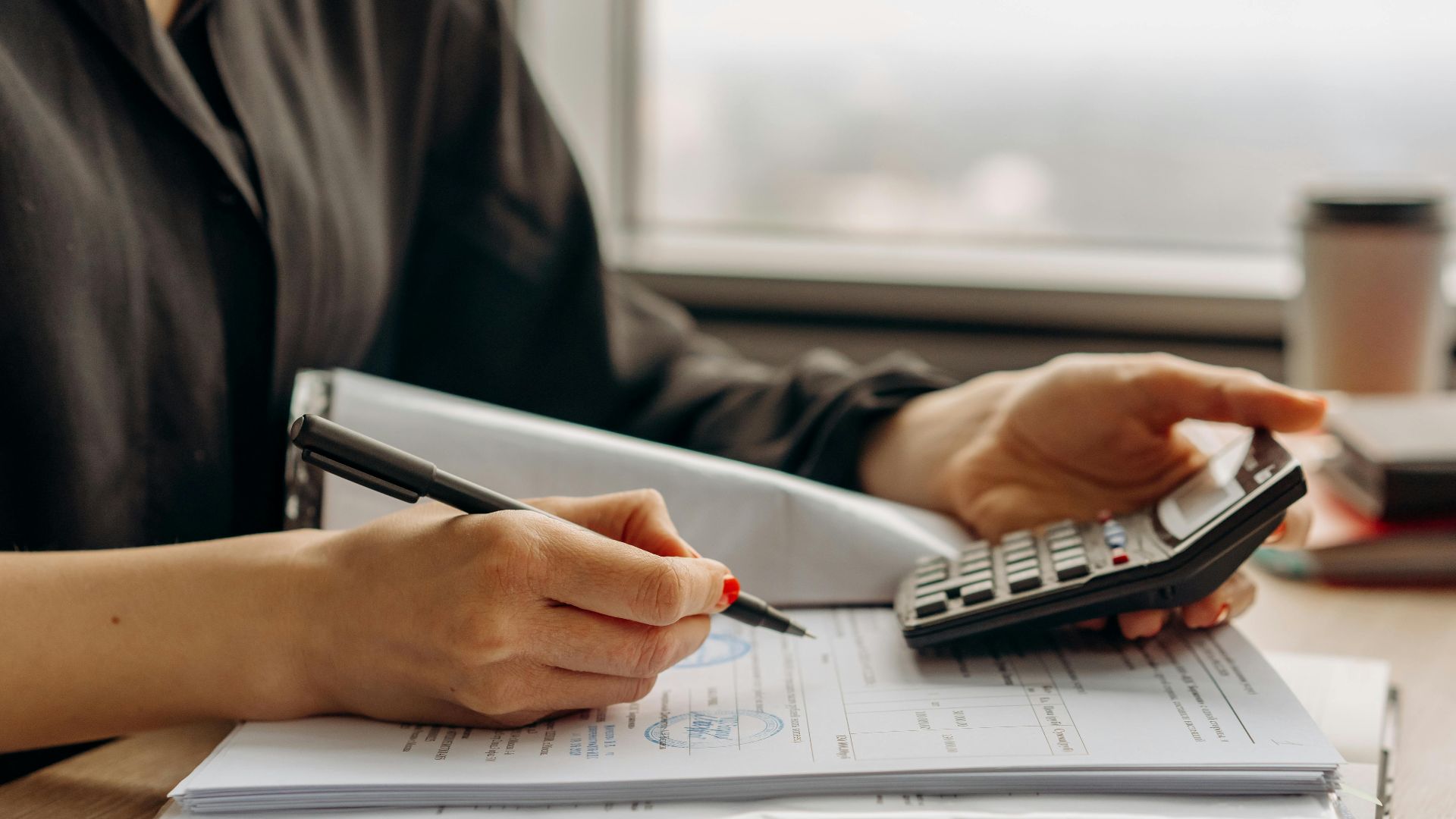 Close-up of person using a calculator with financial documents in an office.