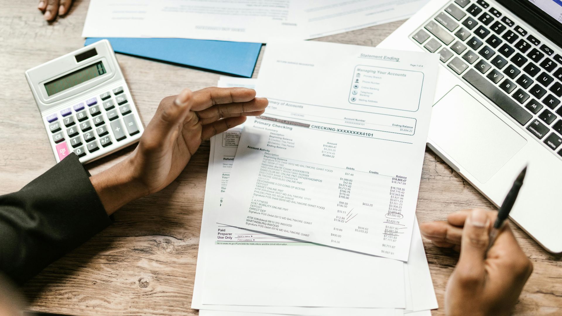 Hands holding financial documents with calculator and laptop on office desk, business analysis scene.
