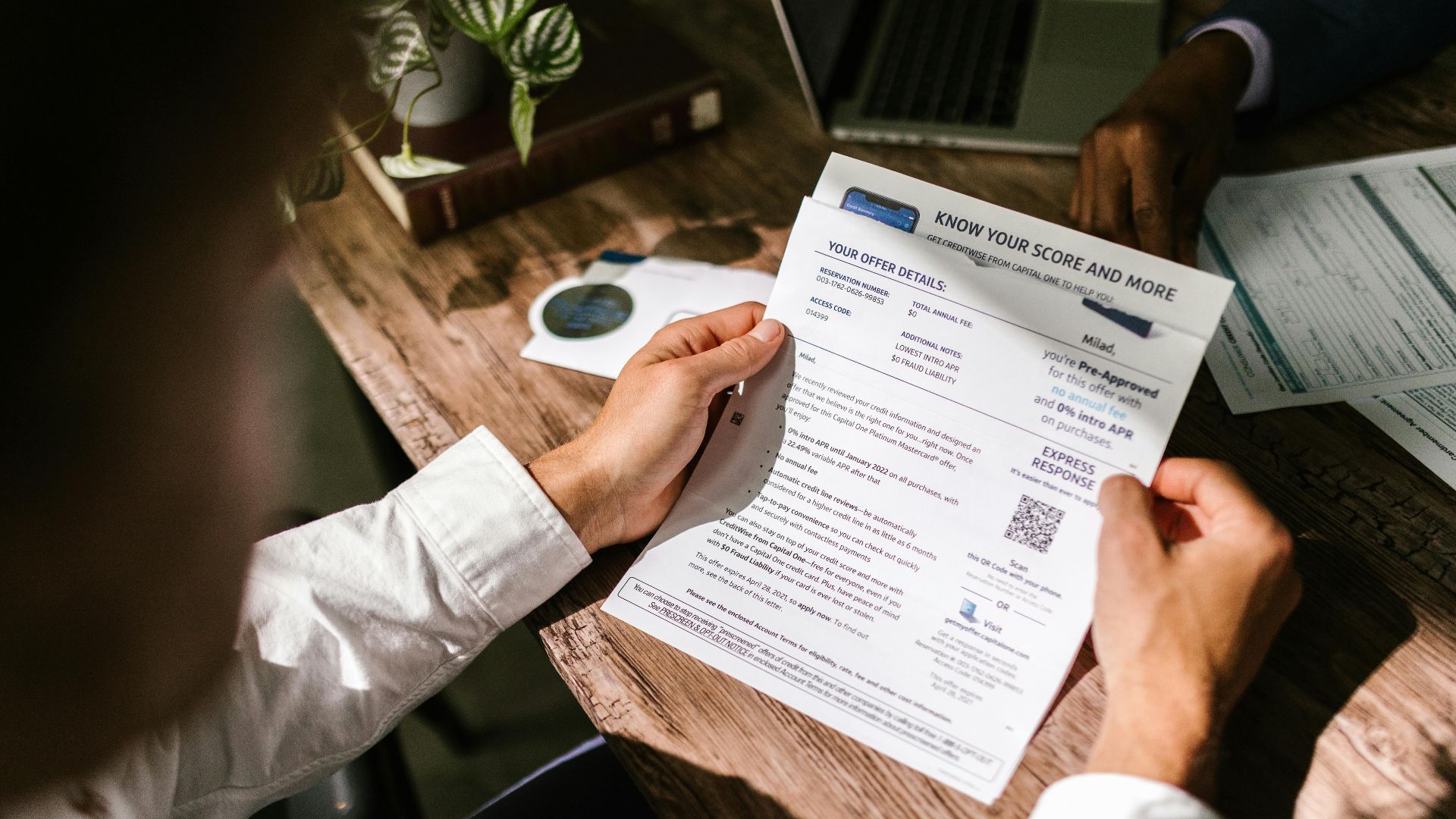 An adult man examining a financial document under natural light at a wooden desk, emphasizing finance and reading.