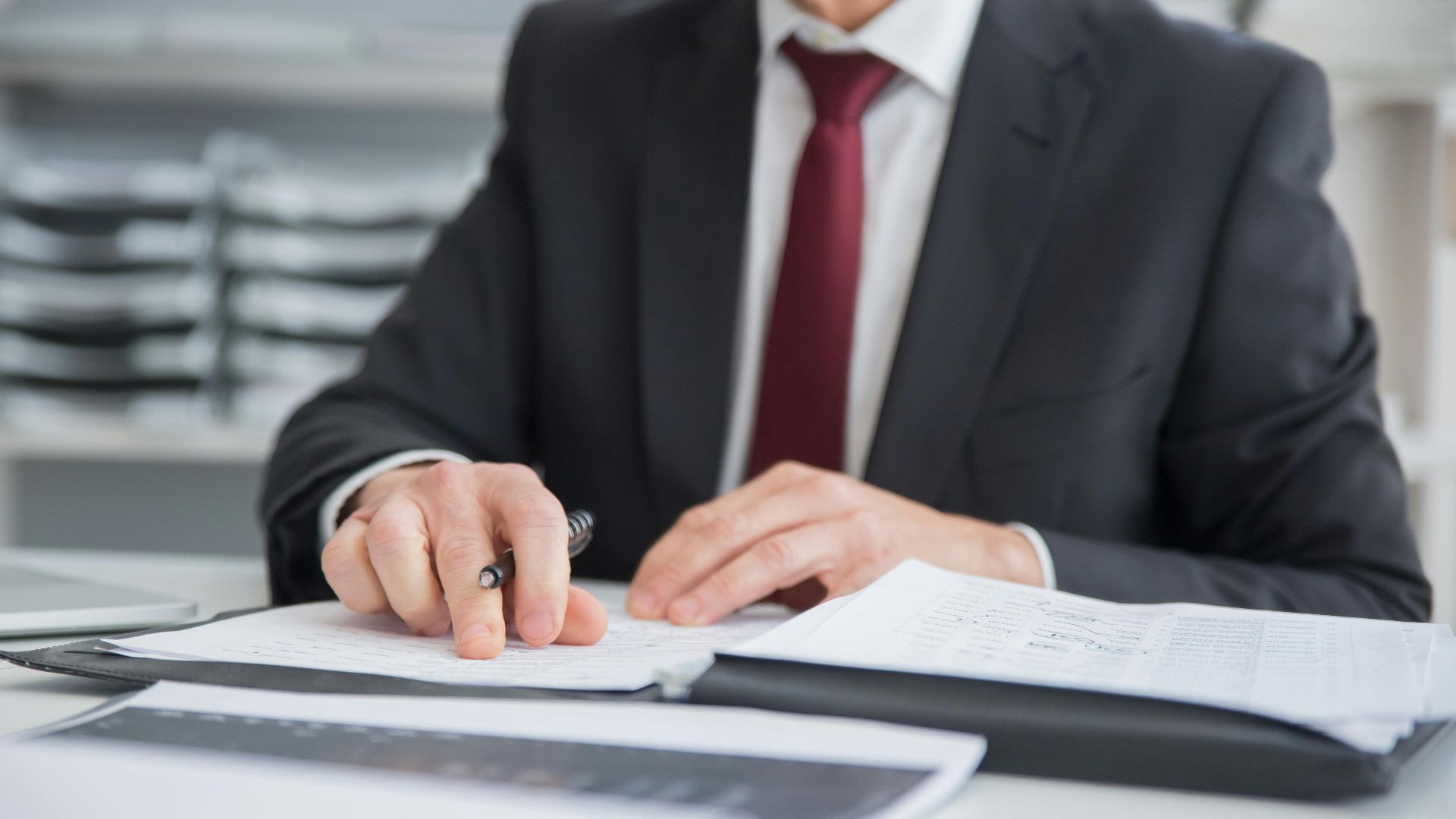 Close-up of a businessman reviewing documents at an office desk. Focus on hands and paperwork.