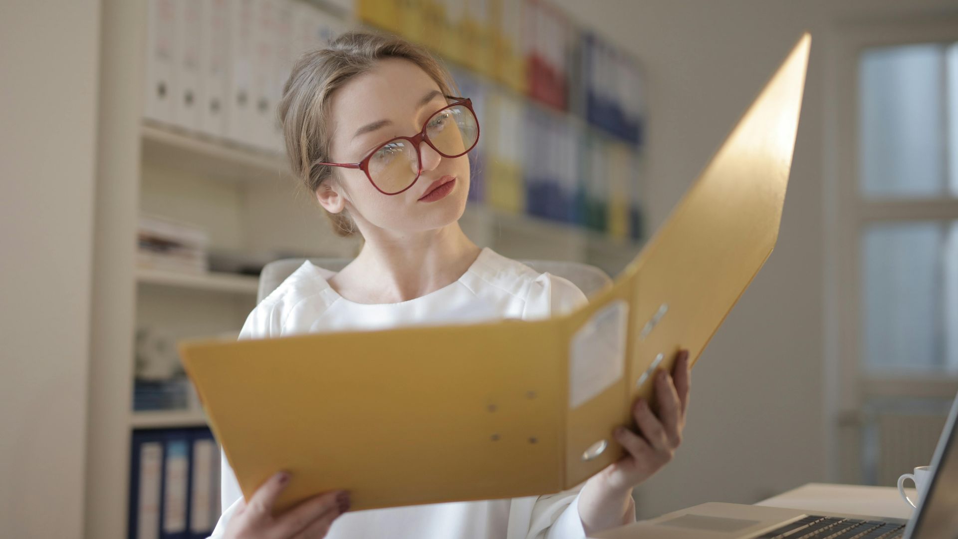 Caucasian woman intensely reading documents in an office setting.
